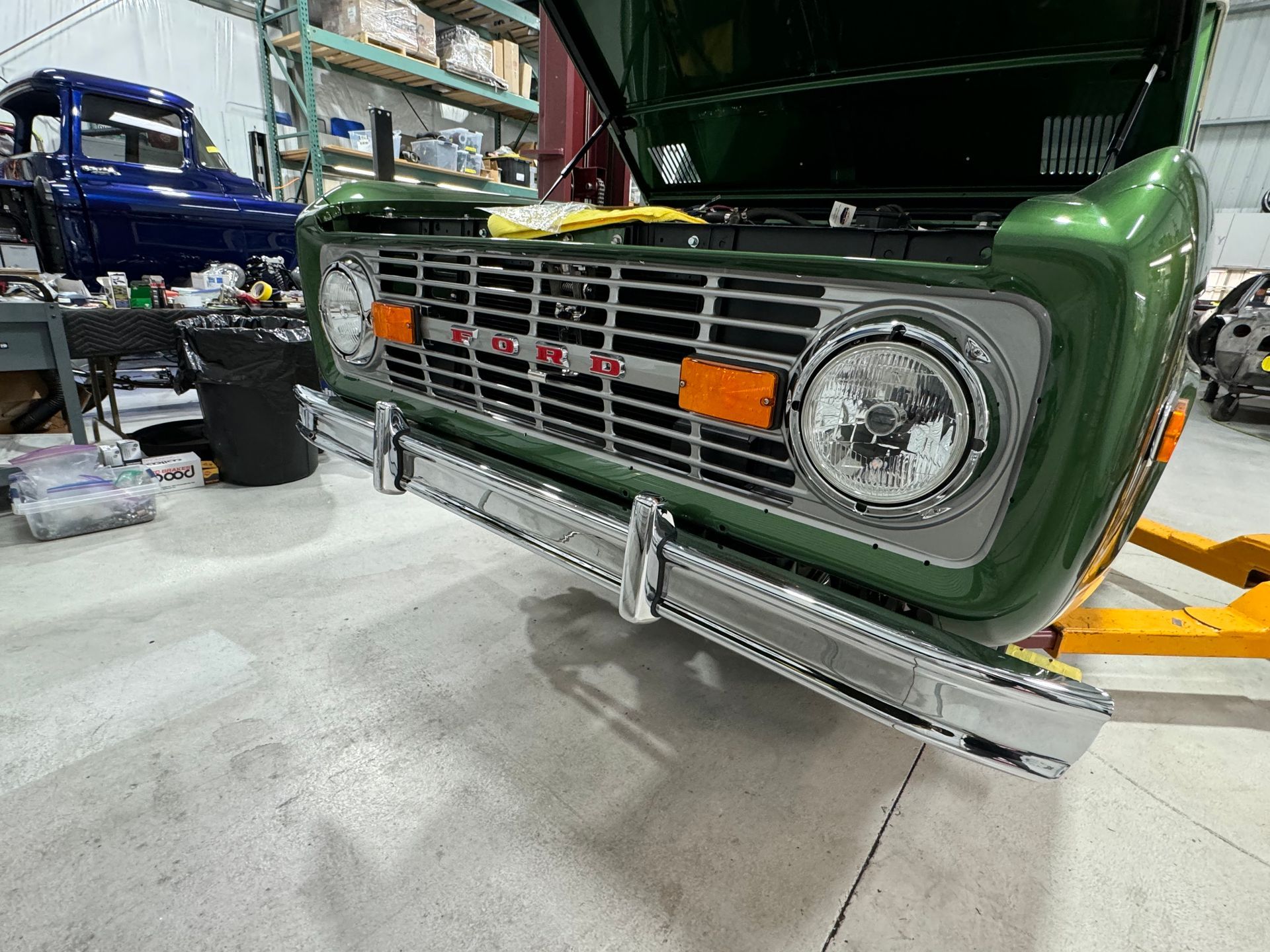 Green classic truck front in a garage, hood open, with chrome grille and round headlight.