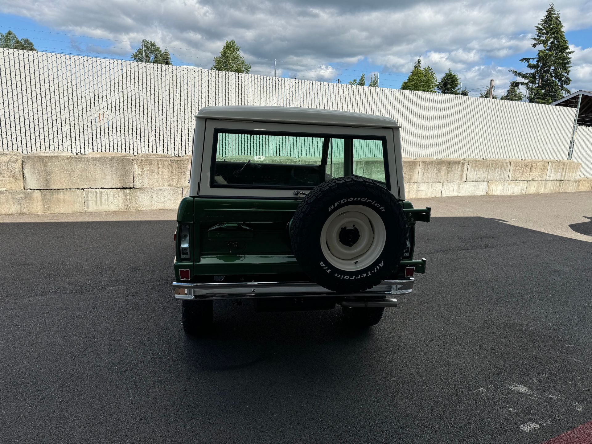 Rear view of a dark green off-road SUV parked on asphalt near a white wall.