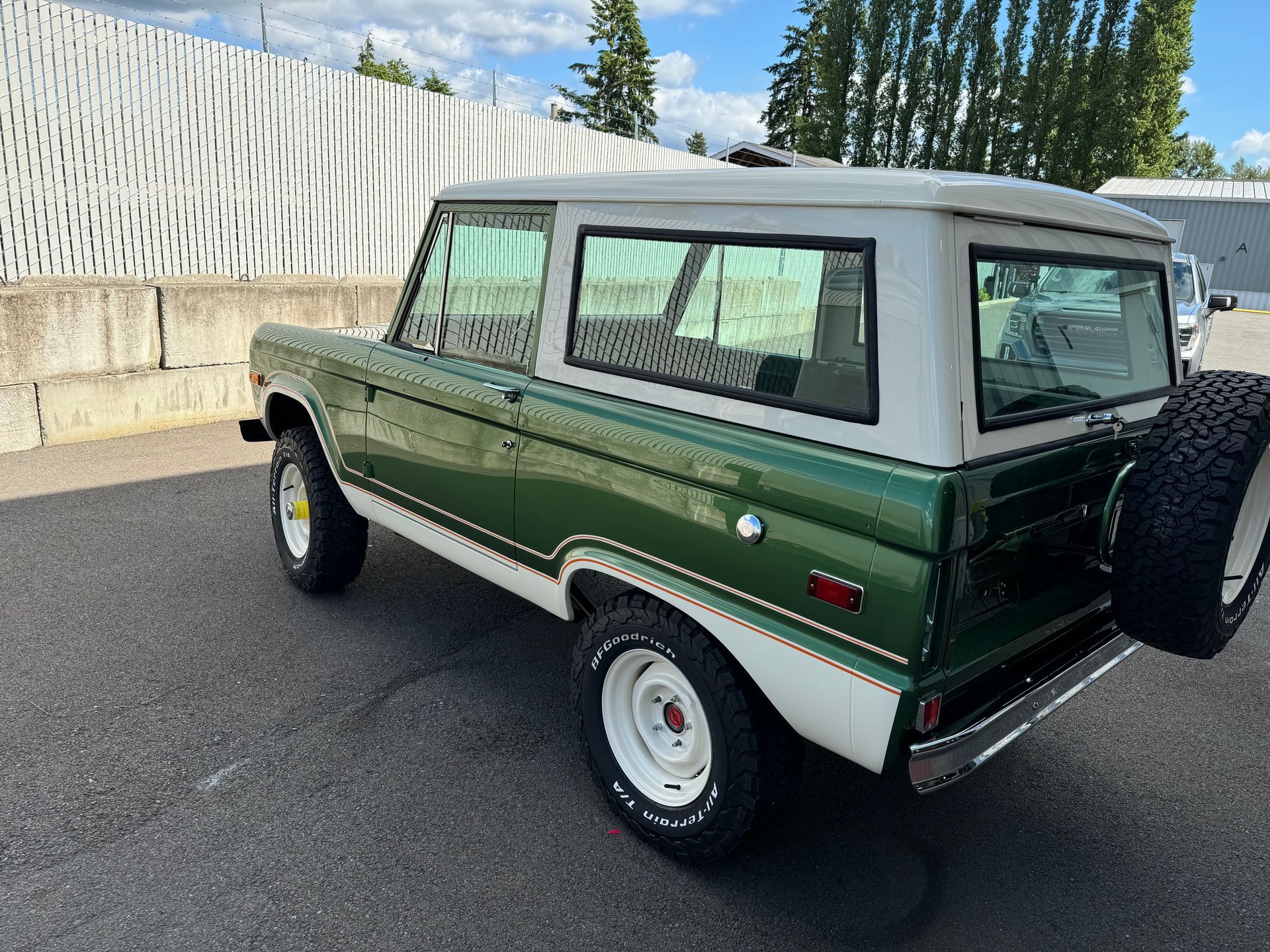 Green vintage SUV parked on pavement beside a fence, with a white roof and spare tire on the back