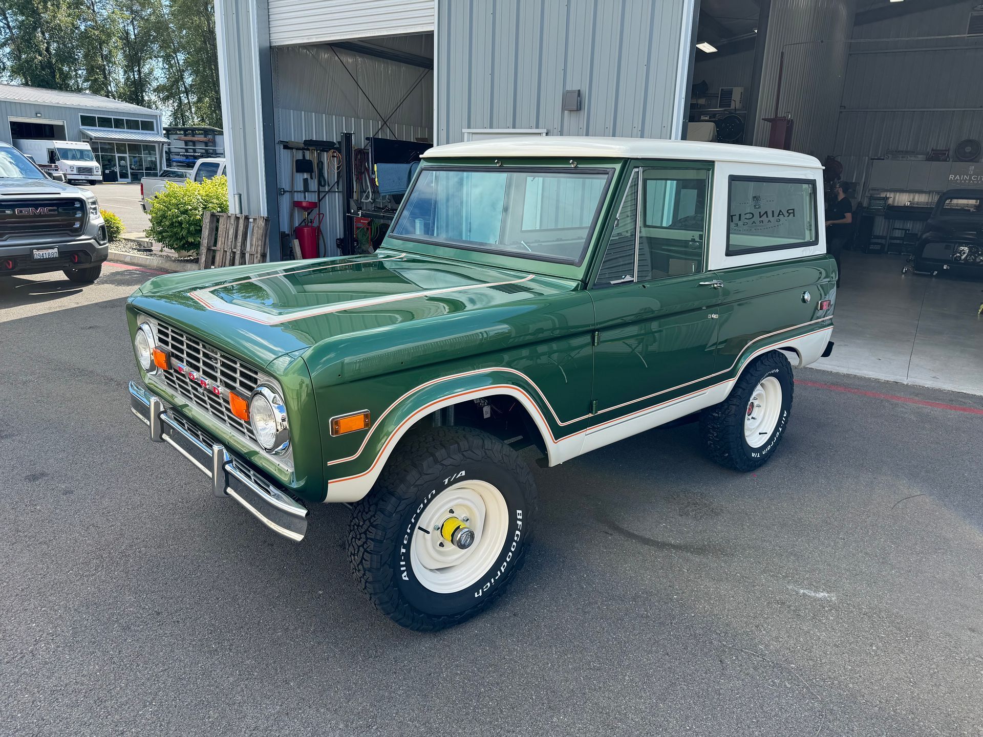 Green classic Ford Bronco parked outside a garage, white roof and off-road tires