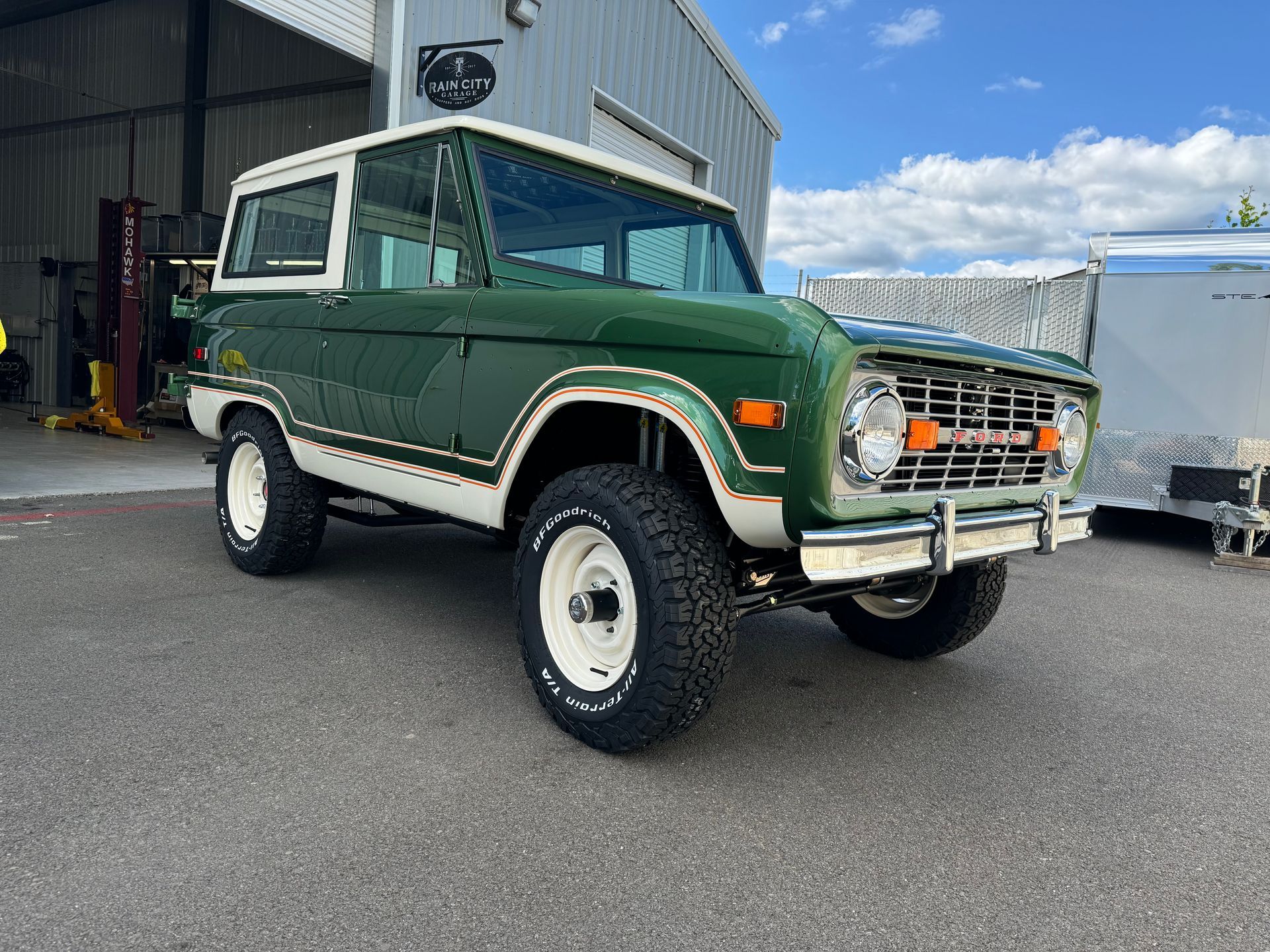 Green vintage Ford Bronco parked outside a garage on an overcast day