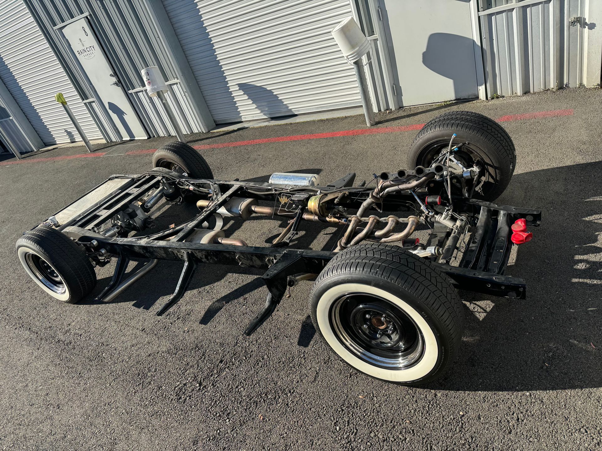 Overturned black chassis of a small vehicle on pavement near a metal fence