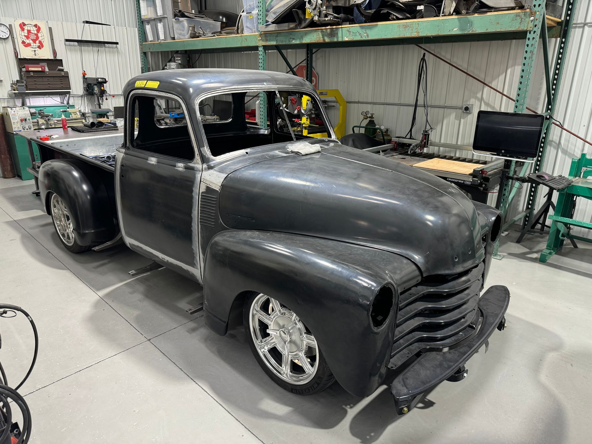 Custom black vintage pickup truck in a workshop, with lowered stance and exposed front grille.