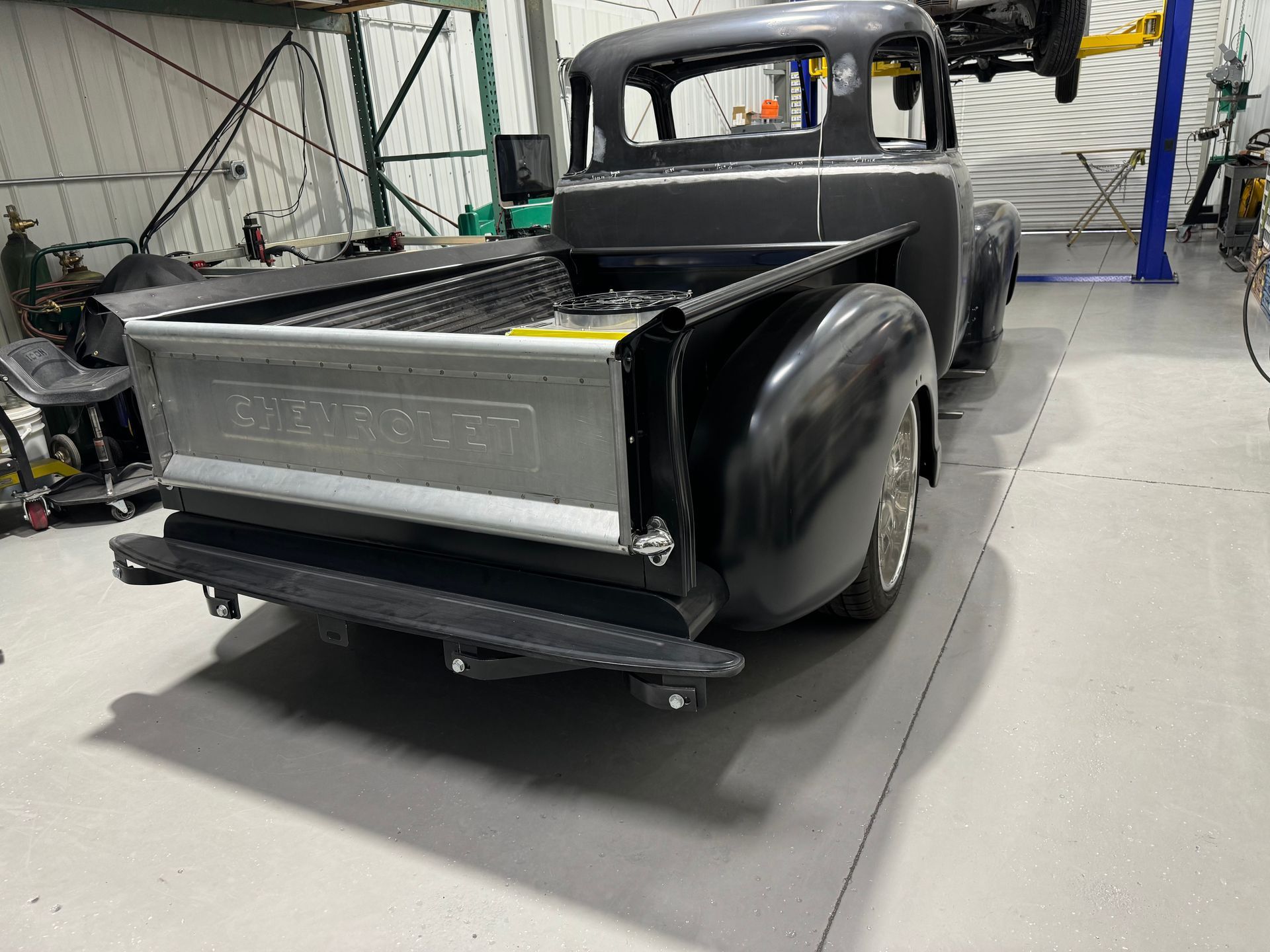 Black vintage pickup truck in a workshop, rear view with open bed and glossy fenders