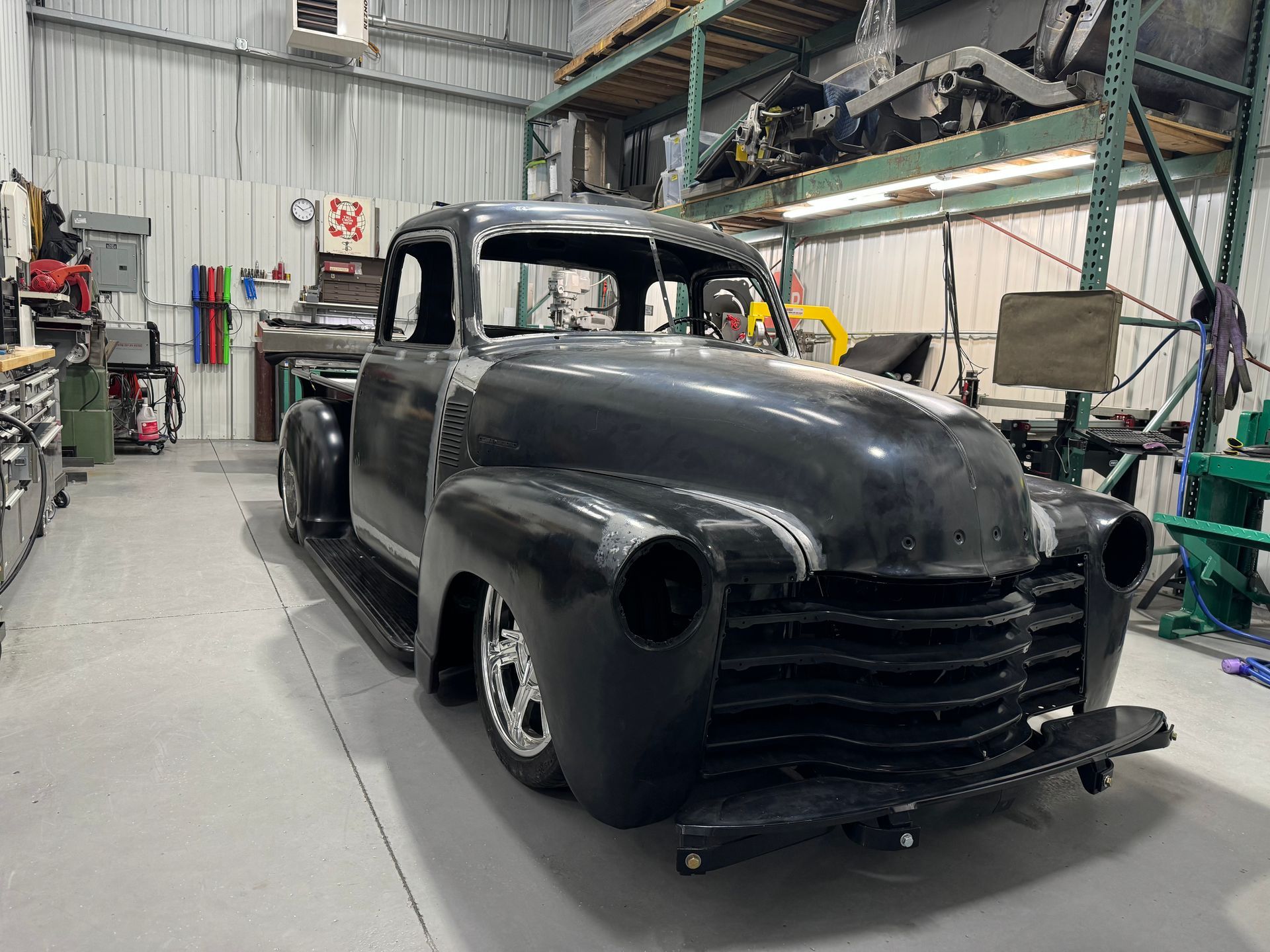 Black vintage pickup truck in a workshop garage, front view, unfinished body with exposed wheels