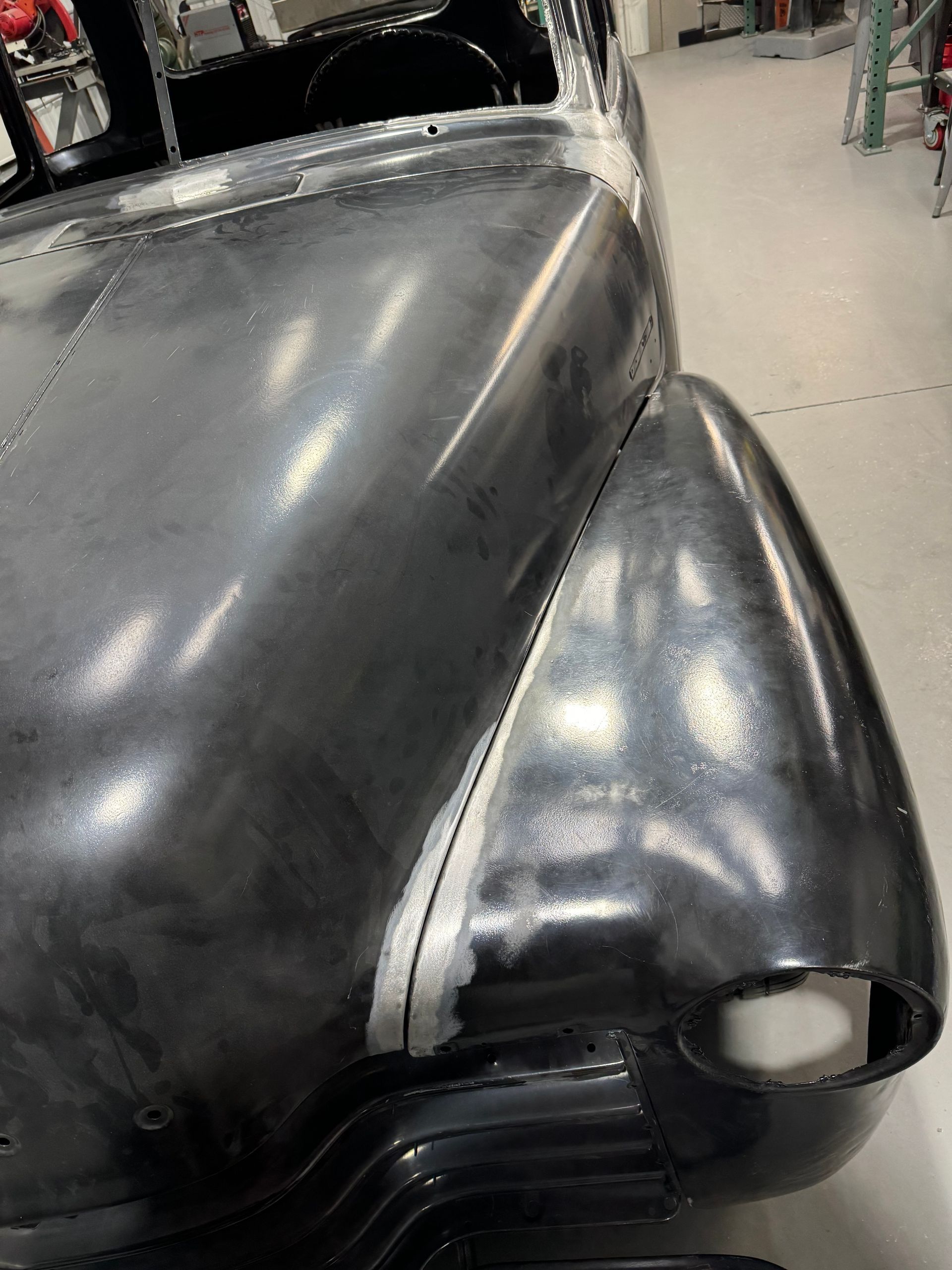 Black classic car front end with rounded fender and hood in a garage workshop