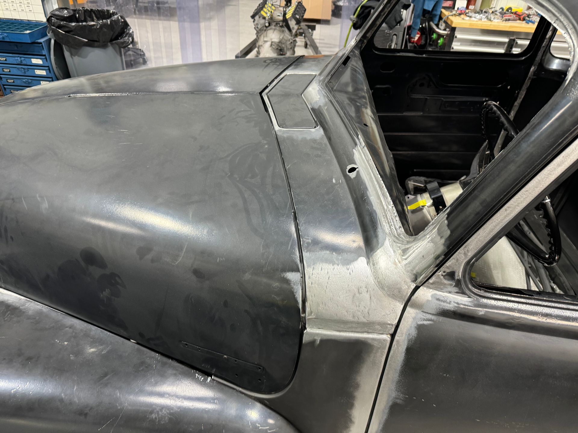 Close-up of a black car body and open side frame in a workshop, with exposed interior.