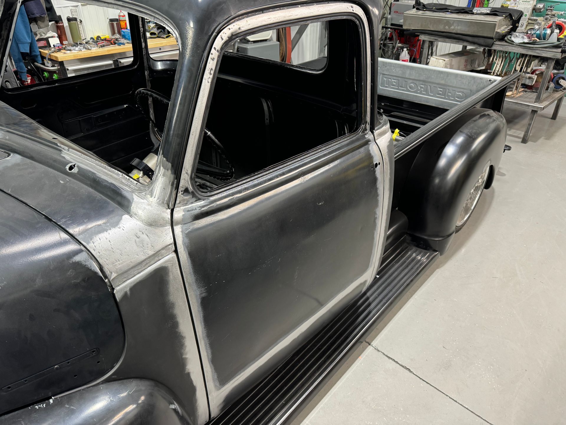 Gray vintage pickup truck cab and bed in a workshop, with partially restored body panels.