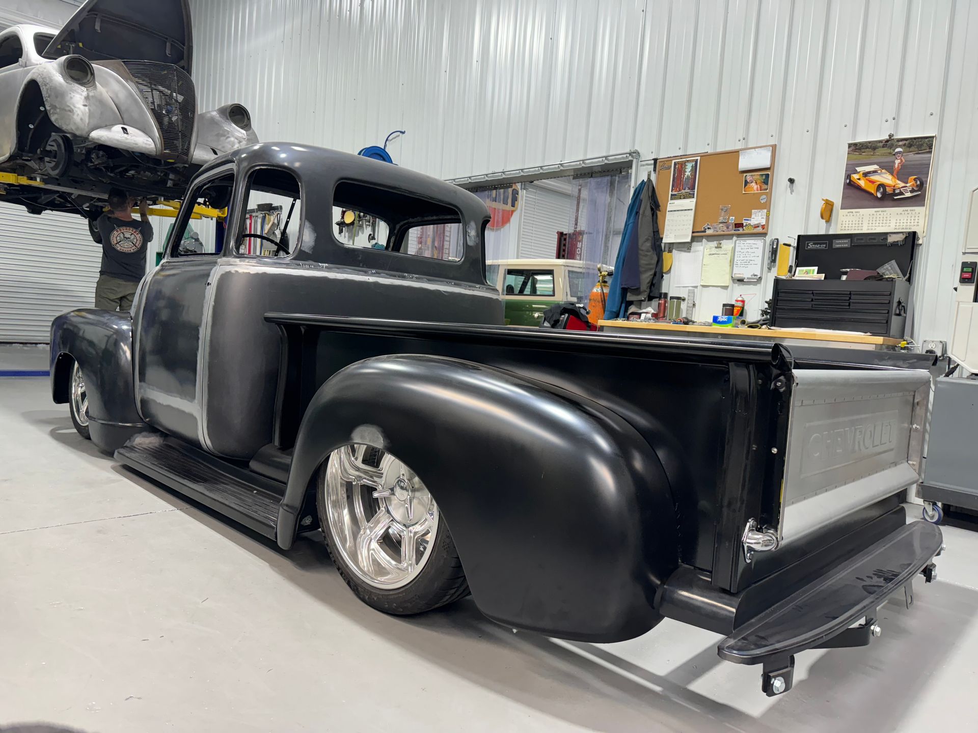 Black custom vintage pickup truck in a garage, with raised hood and polished chrome wheels.