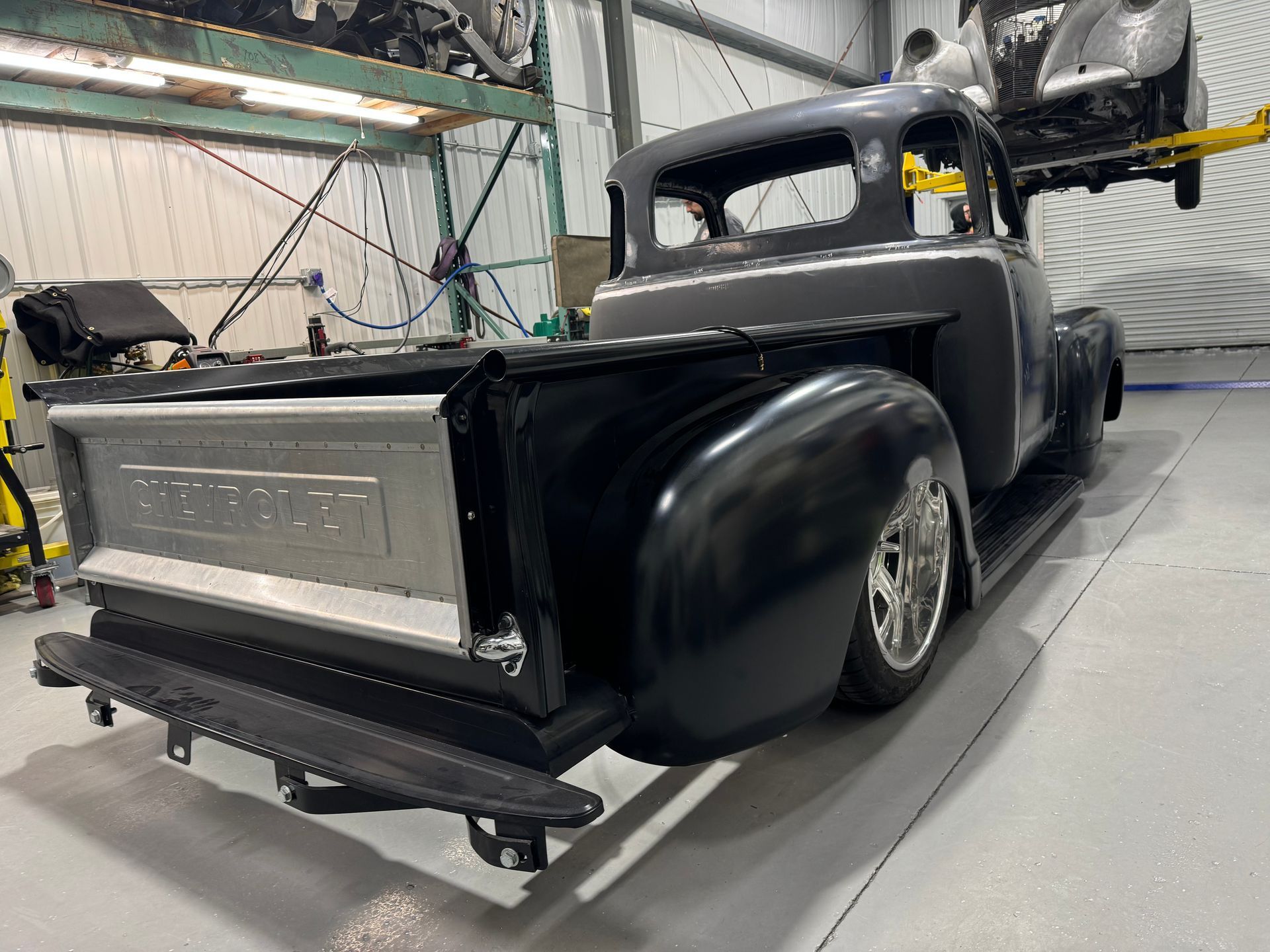 Black vintage pickup truck in a workshop, rear view with a silver tailgate and lowered suspension
