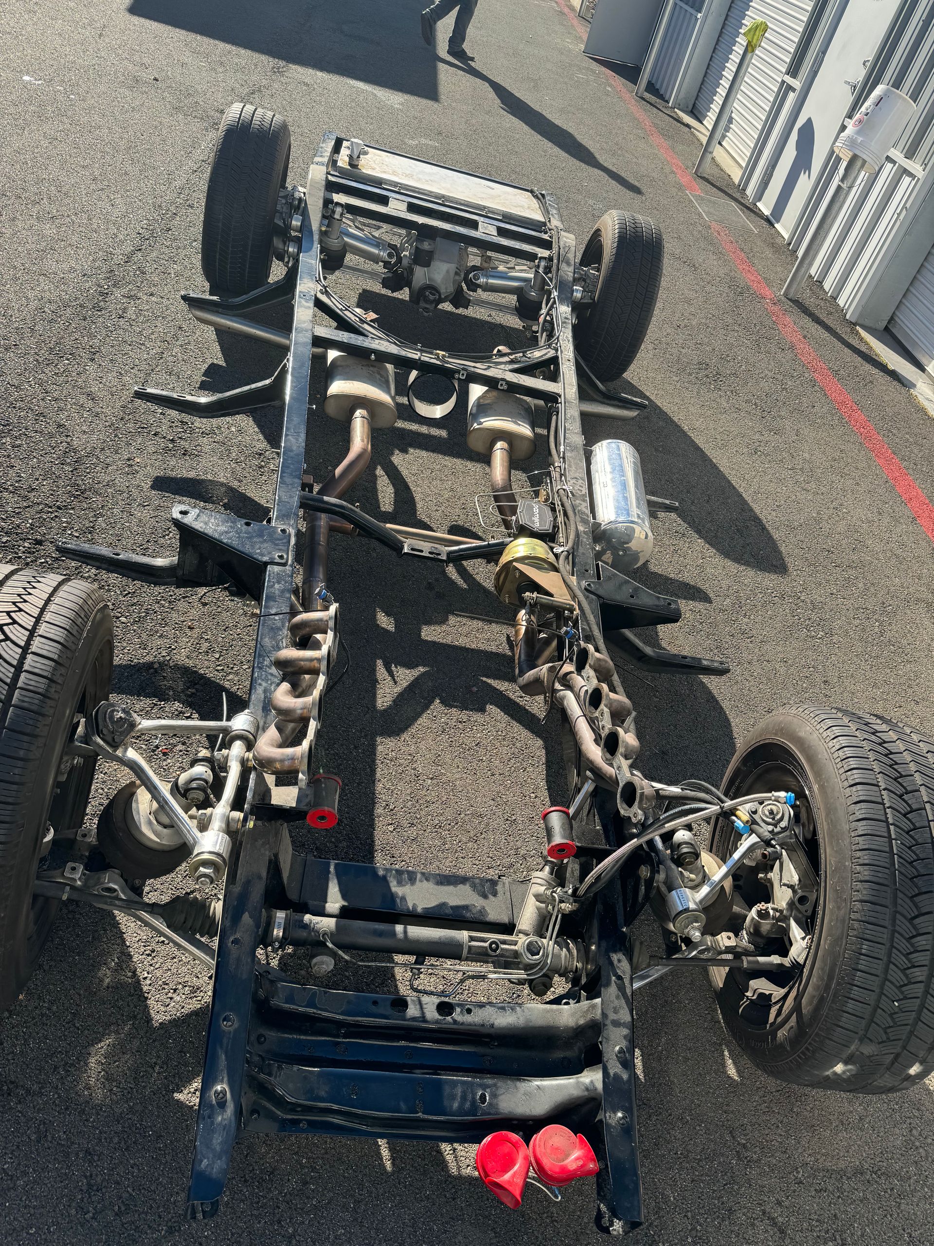 Overturned go-kart chassis on asphalt, with exposed frame, wheels, and parts scattered nearby.