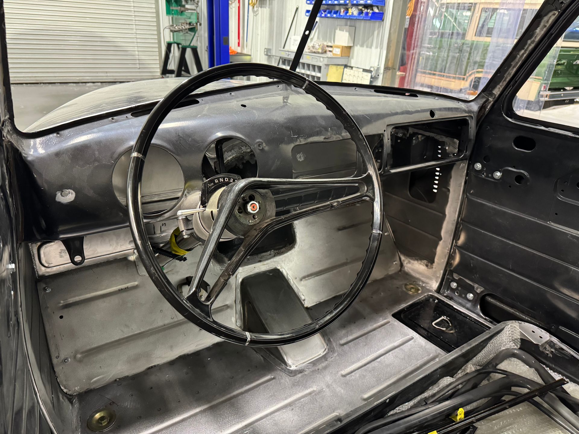 Interior of a stripped black car with bare metal panels, steering wheel, and racing bucket seat