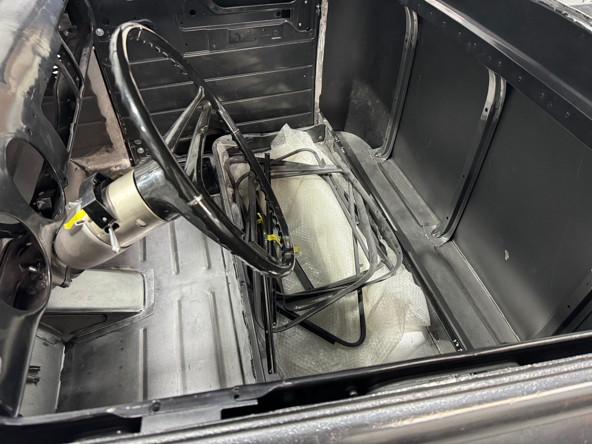 Car interior stripped for repair, with exposed steering wheel, wiring, and removed seats