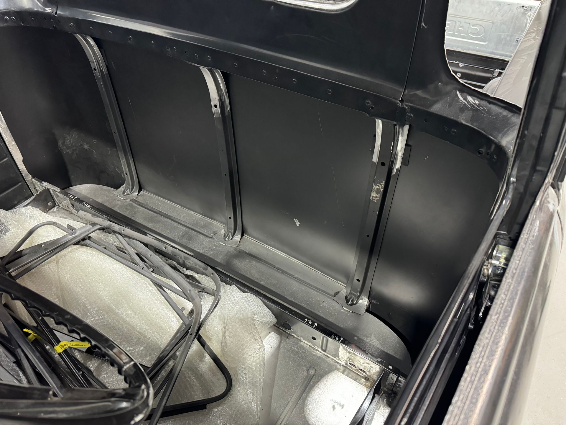Black painted car trunk interior with exposed panels and loose parts on the floor