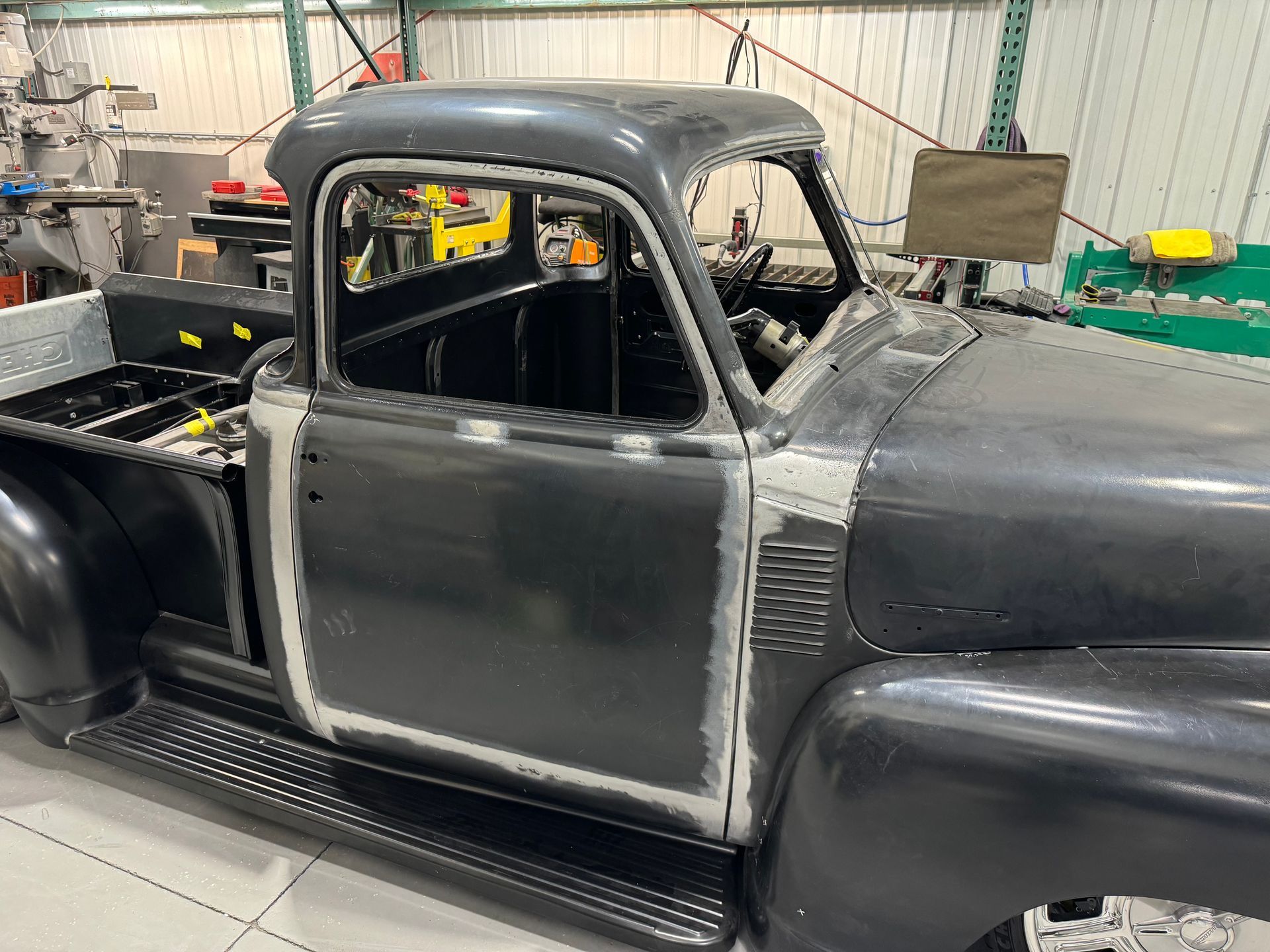 Black vintage pickup truck cab in a workshop, partially painted and undergoing restoration.
