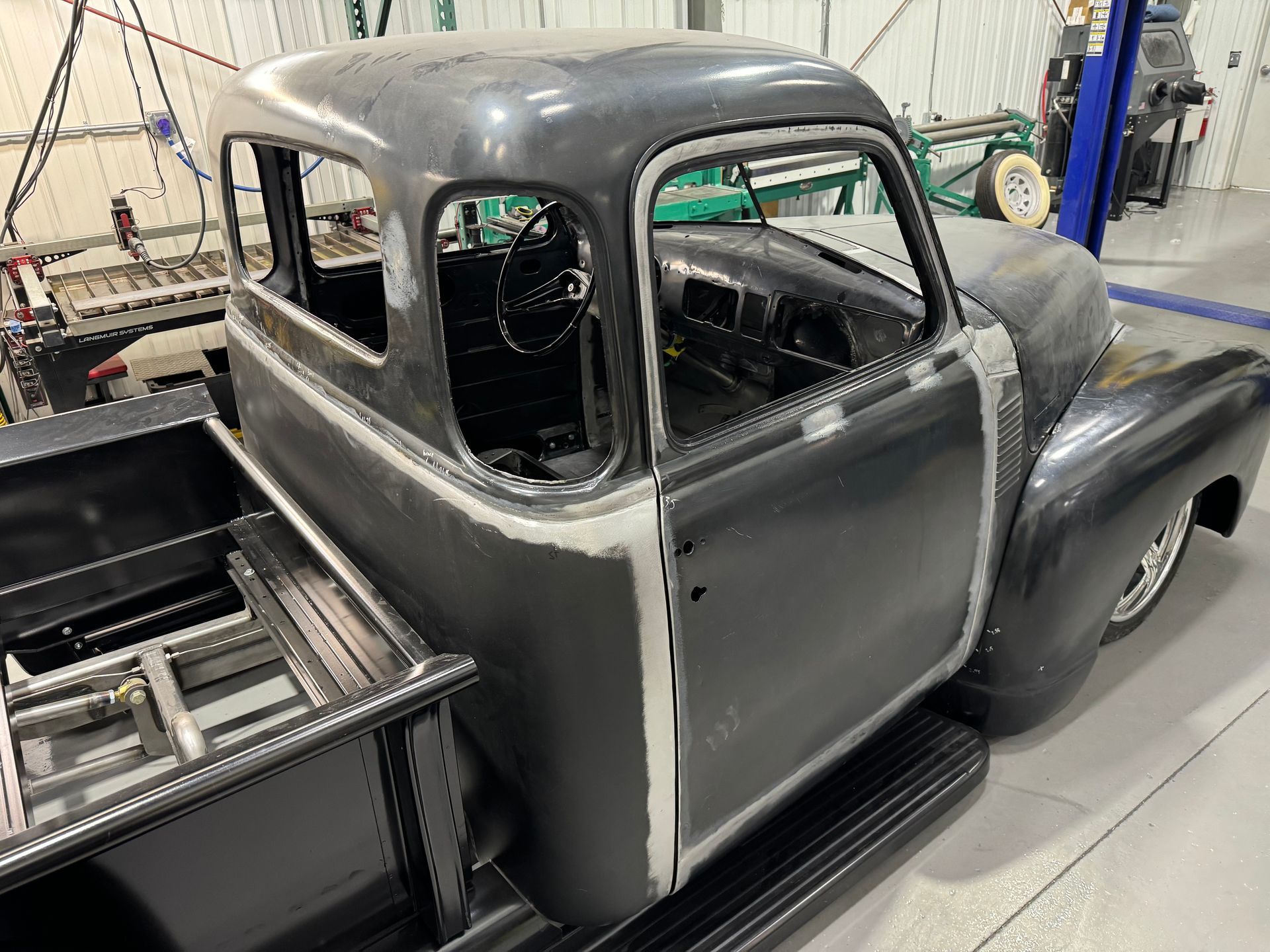 Partially restored black vintage pickup truck in a workshop, with primer-gray doors and open cab interior