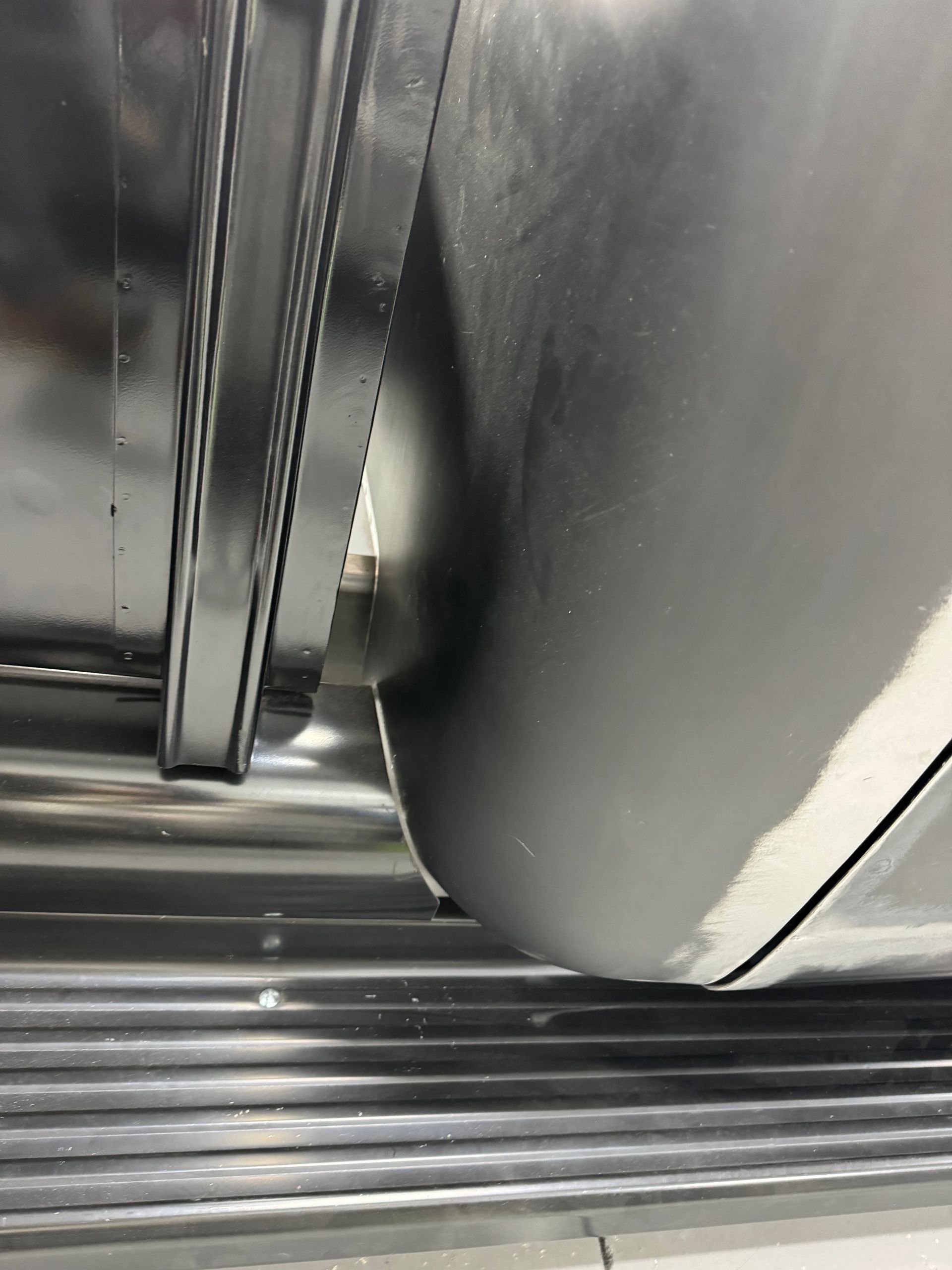 Close-up of a metal stair or conveyor surface with black curved panels and a narrow gap between parts