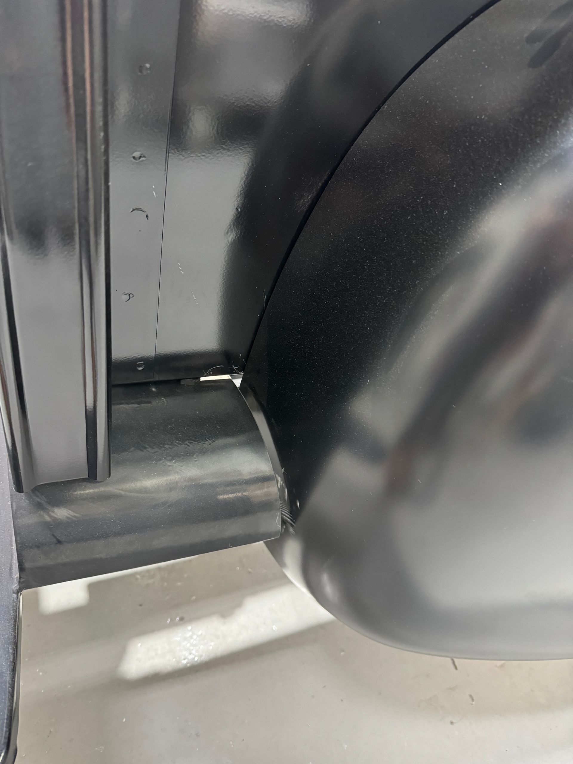 Close-up of a black plastic wheel or knob beside a metal frame on a white surface.