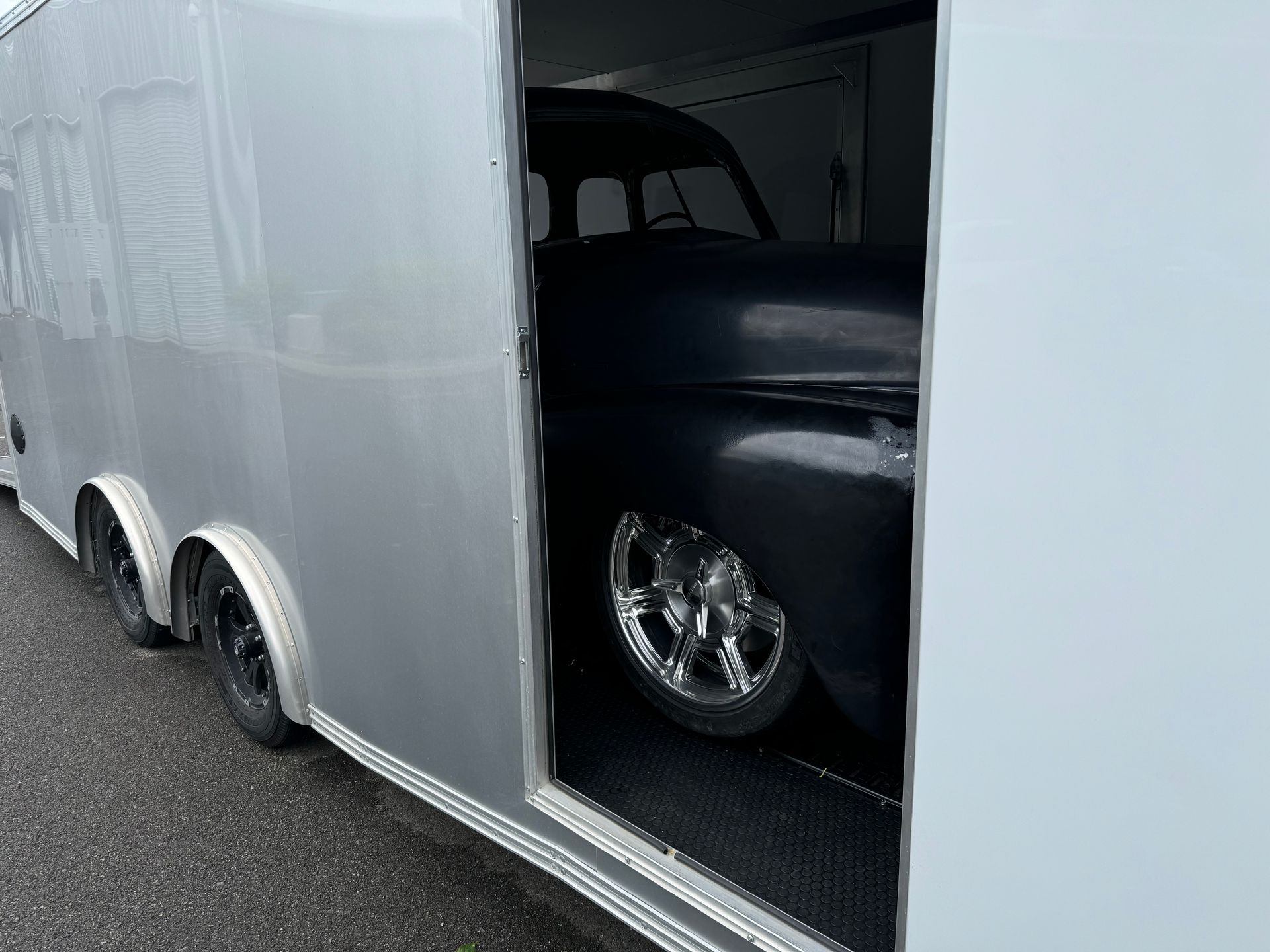 Black classic car inside a silver enclosed trailer, viewed through the open side door