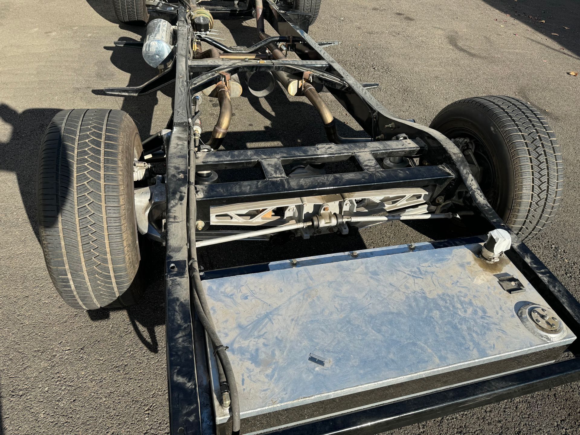 Damaged vehicle chassis with exposed frame and wheels on a paved surface, viewed from above