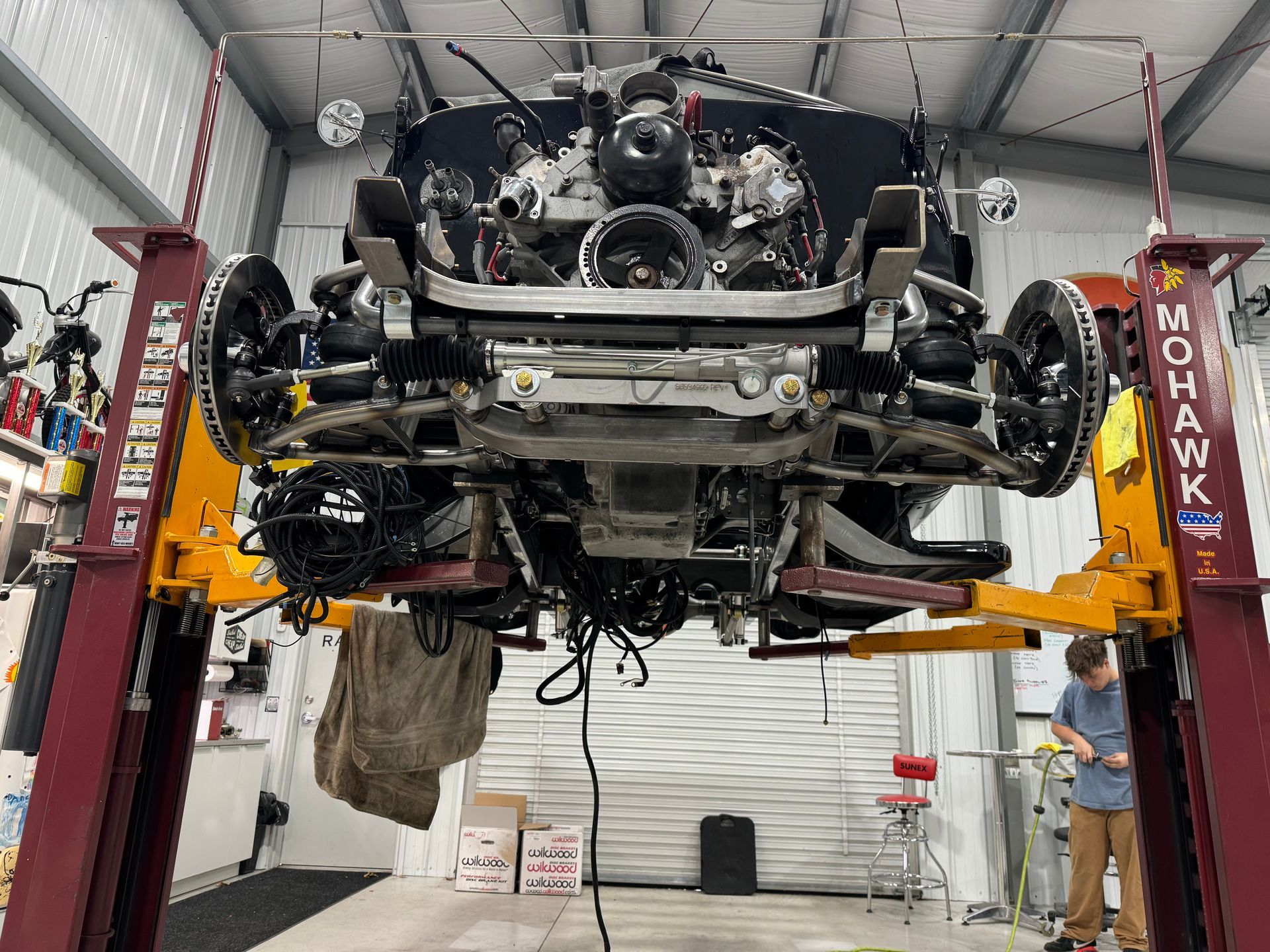 Undercarriage of a suspended car in an auto shop lift, with mechanics nearby.