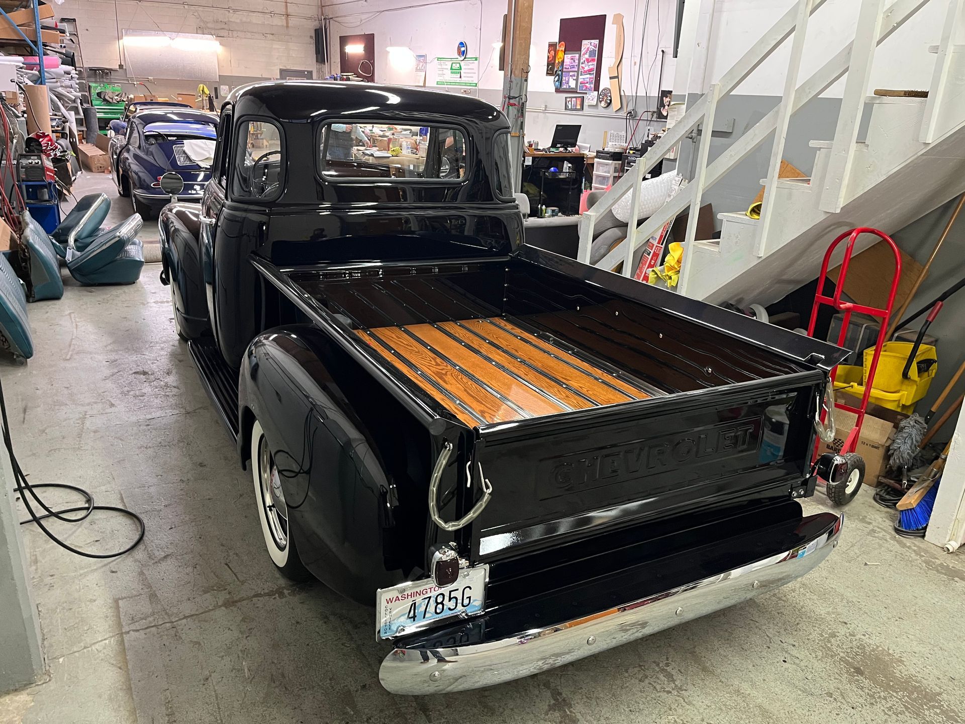 Black vintage pickup truck in a garage, viewed from the rear with a wooden truck bed.