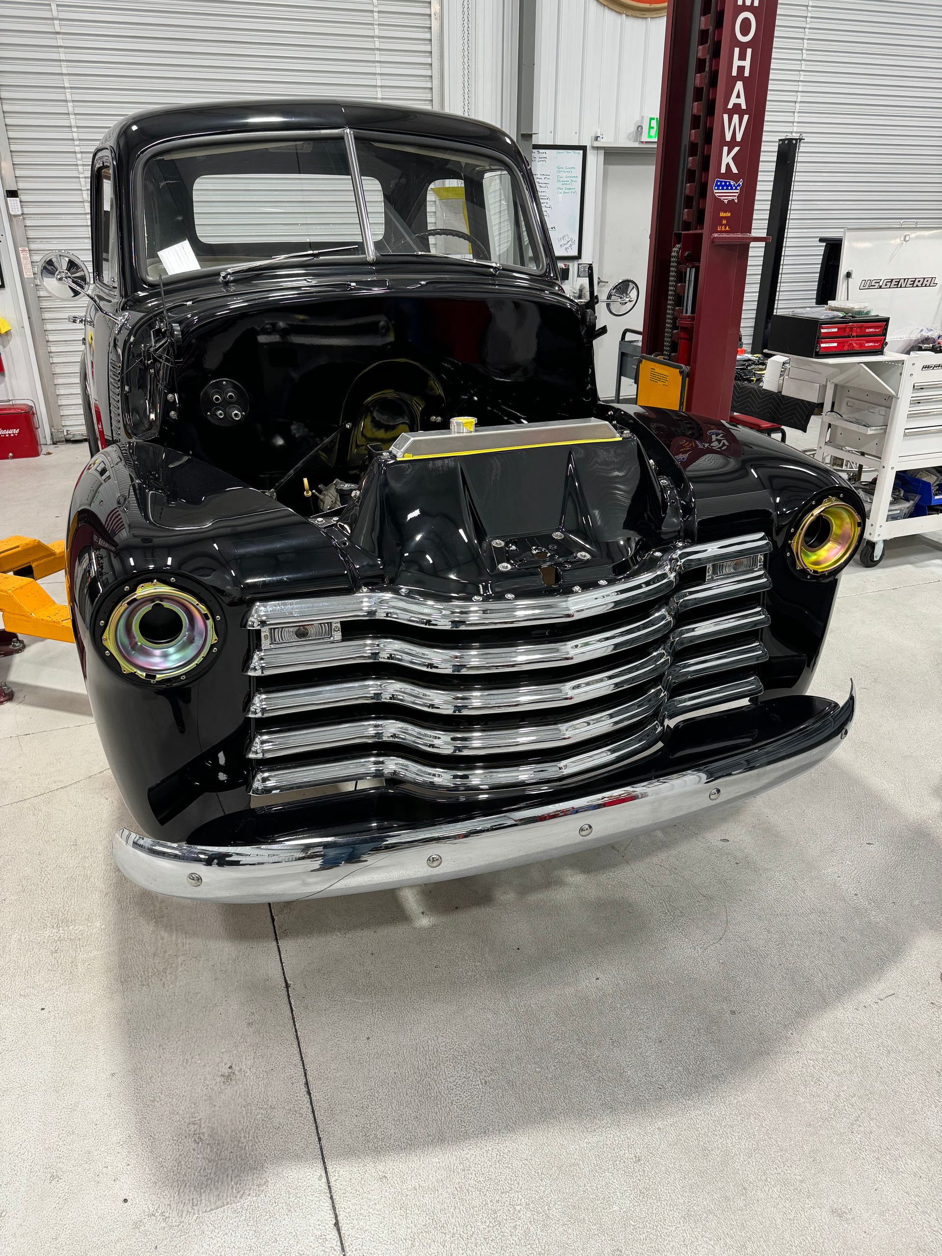 Black vintage truck front end in an auto shop, with chrome grille and headlight surrounds exposed
