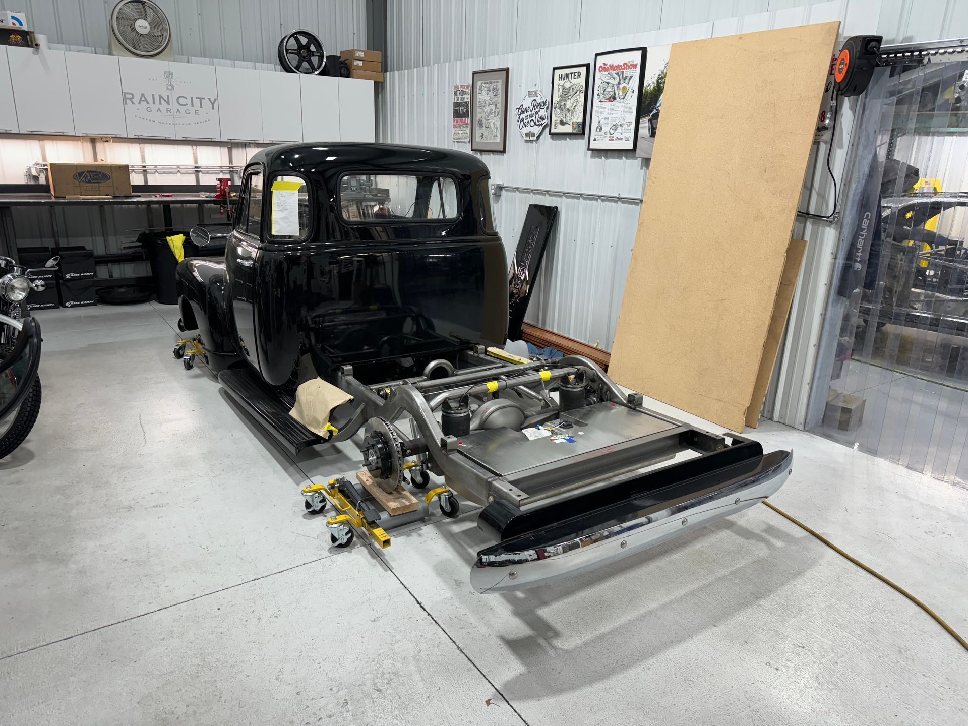Black car body shell on a chassis in an auto workshop, with tools and panels nearby