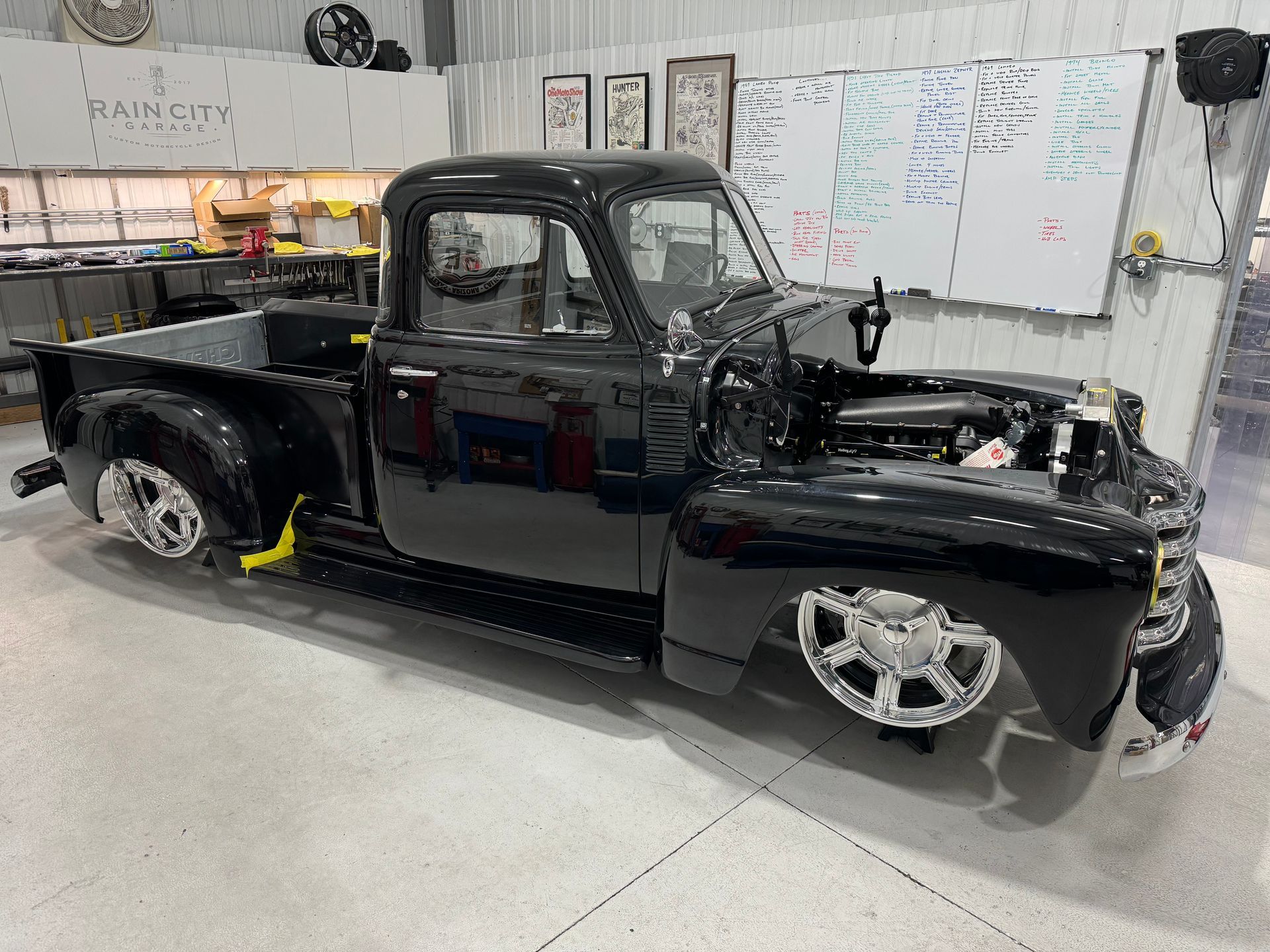 Black vintage pickup truck in a garage, with open hood and chrome wheels