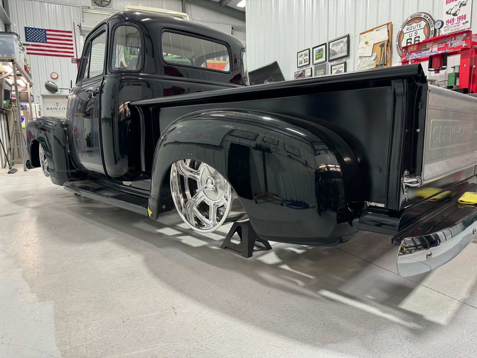 Black classic pickup truck in a garage, with shiny chrome wheels and a long bed.