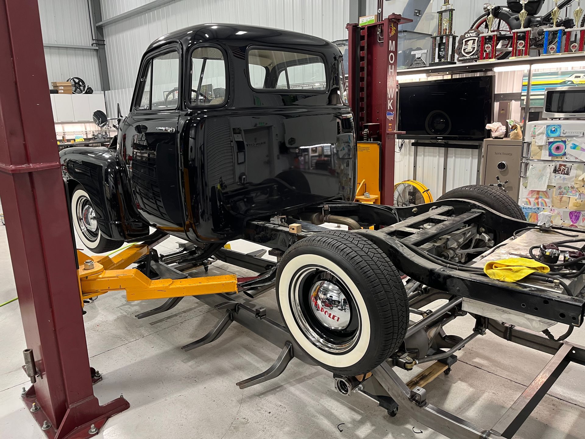 Partially restored black vintage pickup truck in a workshop on a chassis frame lift