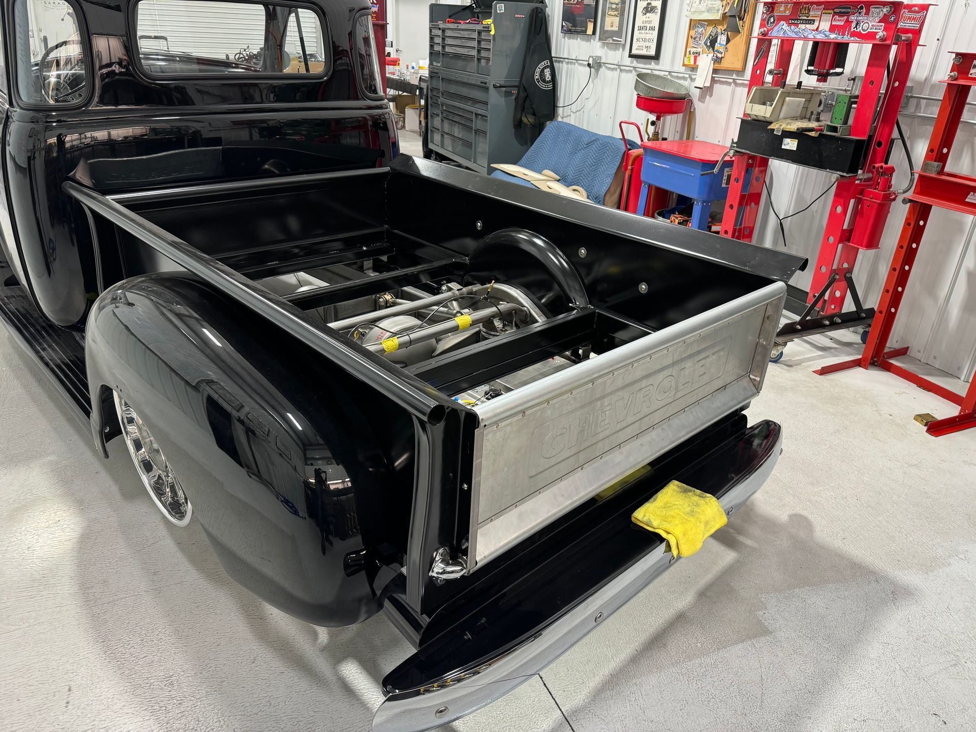 Black vehicle with rear cargo area exposed in an auto shop, showing a bare frame and open tailgate.