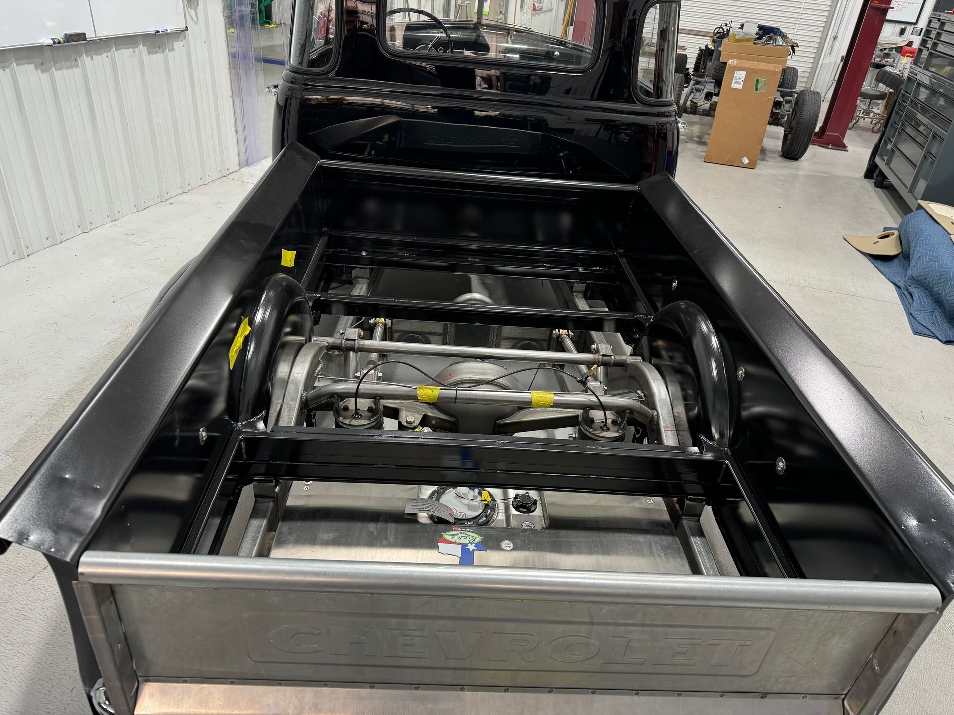 Black pickup truck bed under construction with exposed frame in a garage workshop