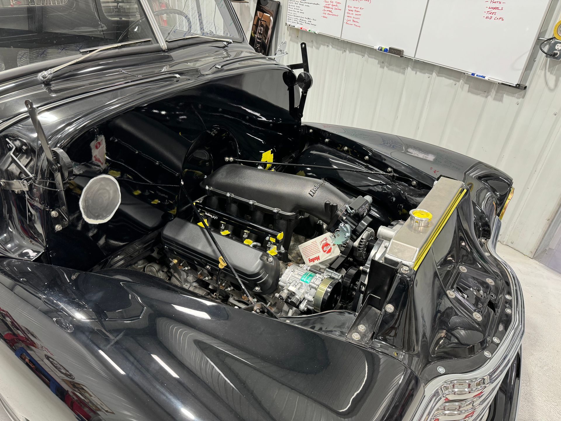 Black sports car with hood open in a garage, showing exposed engine components.