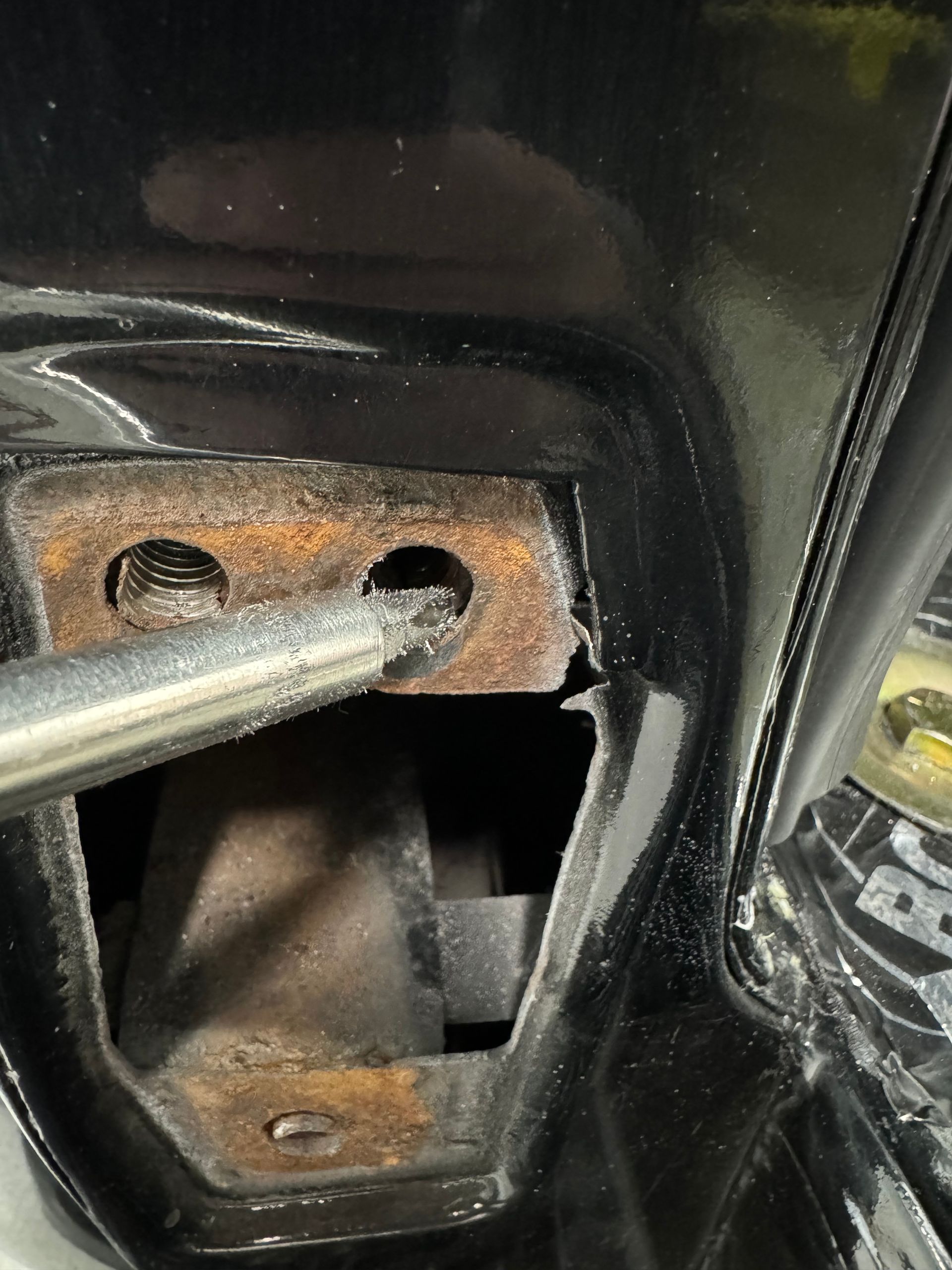 Close-up of a rusty metal latch mechanism with a rod inserted into a black painted housing.