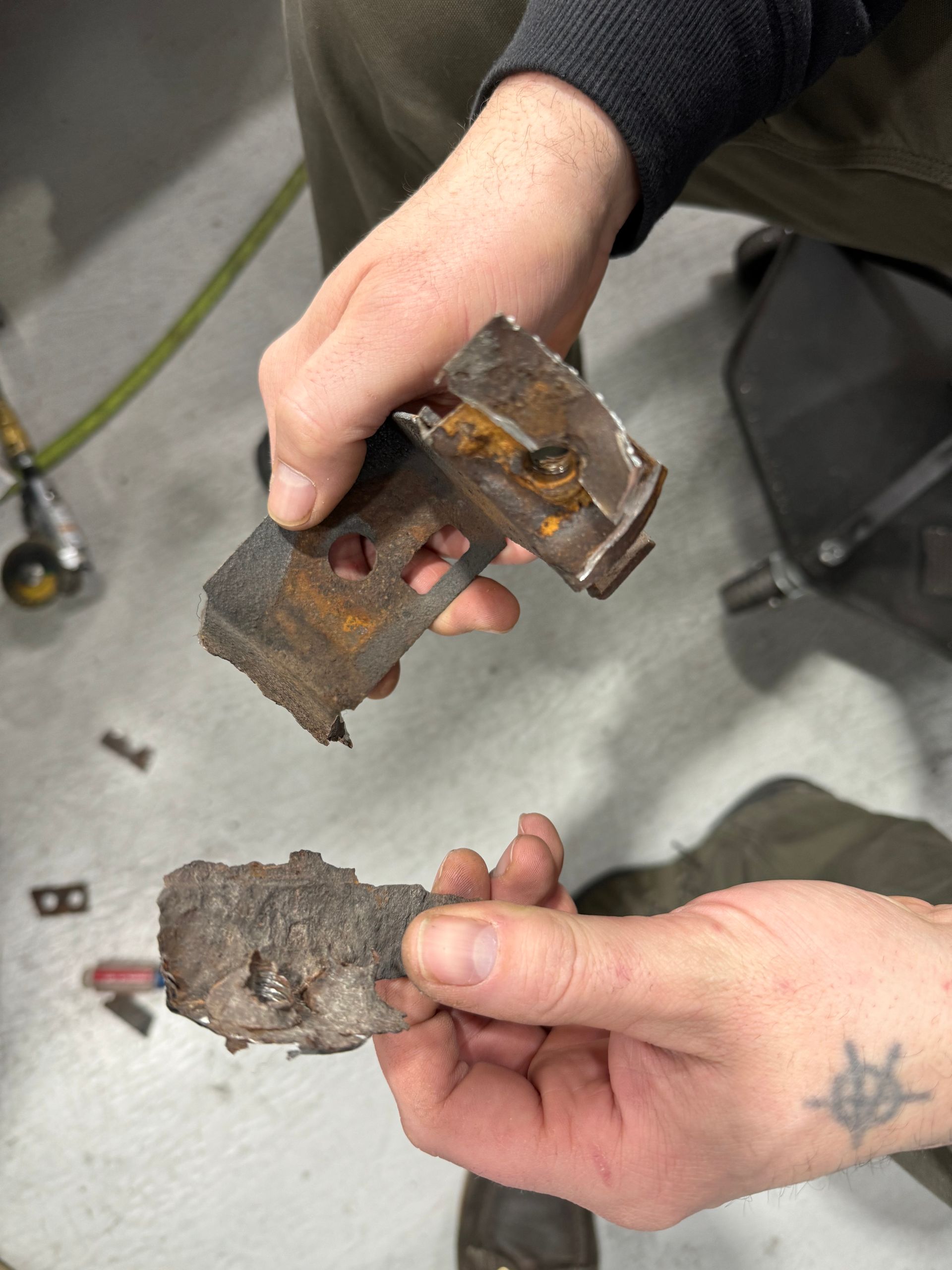 Hands holding two rusty metal fragments over a gray floor.