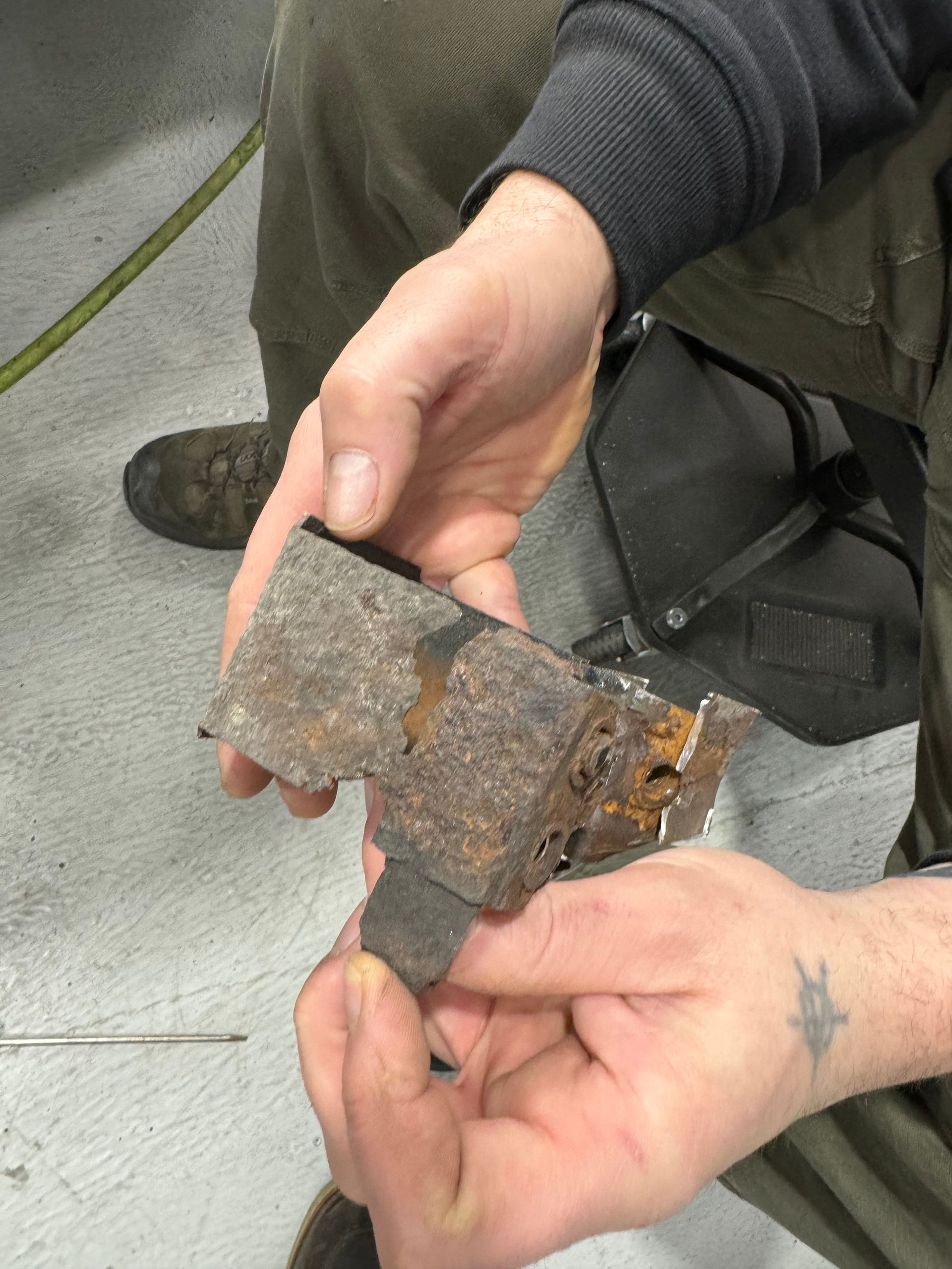 Hands holding a rusty metal fragment over a gray sidewalk.