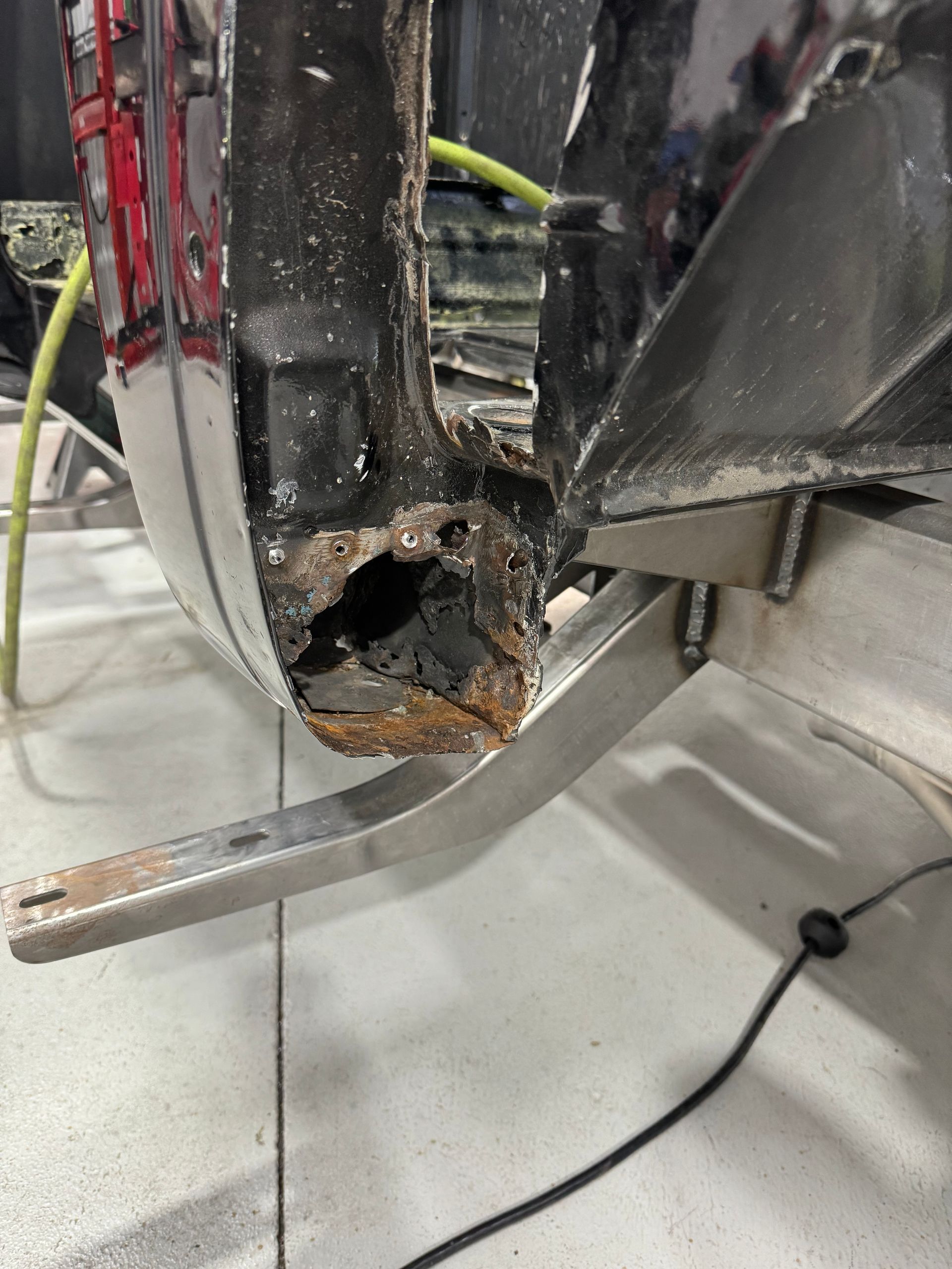 Damaged black metal frame with a large rusted hole and exposed interior wiring in a workshop setting