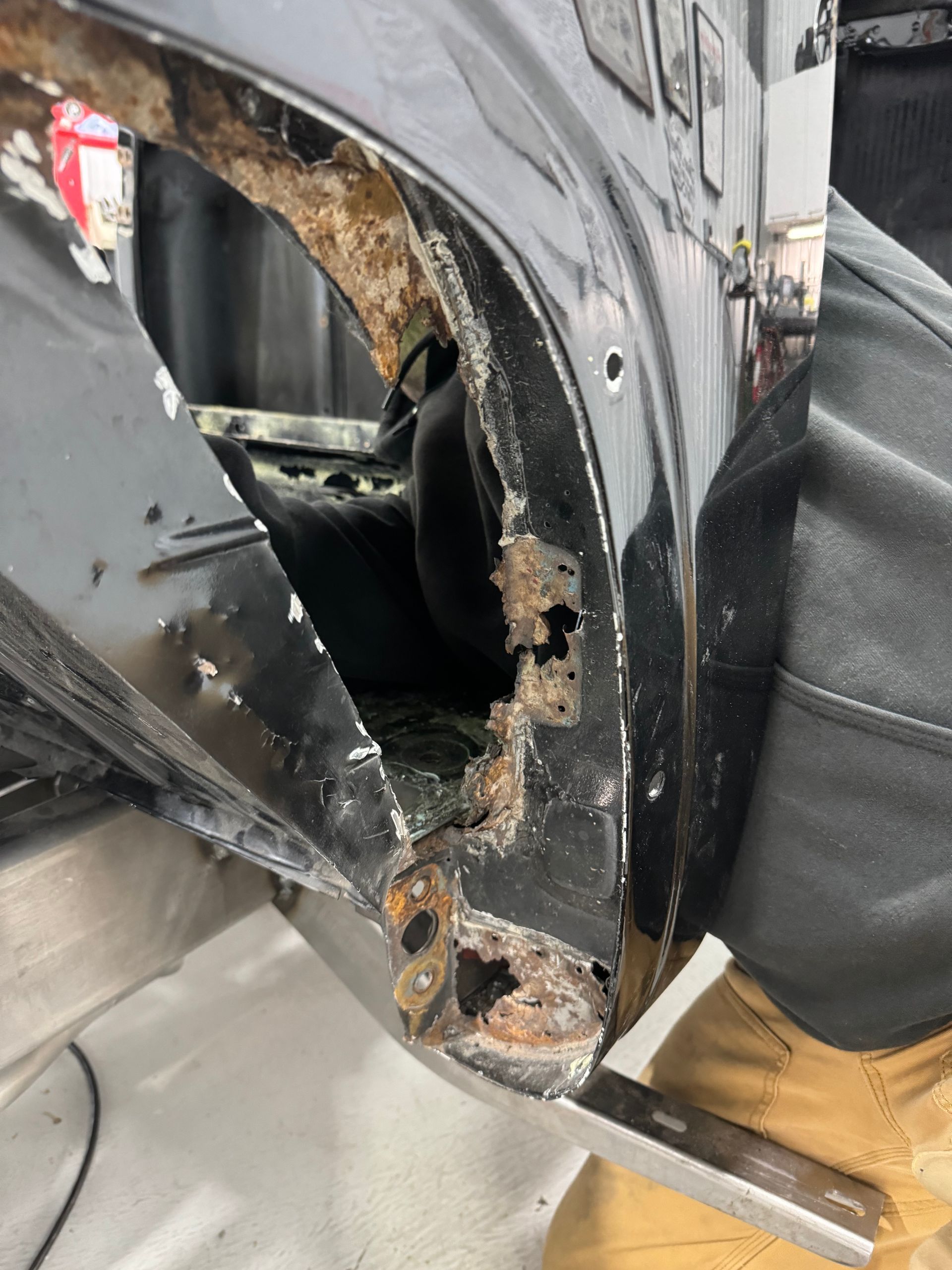 Damaged car body panel with rusted, jagged hole near the wheel well