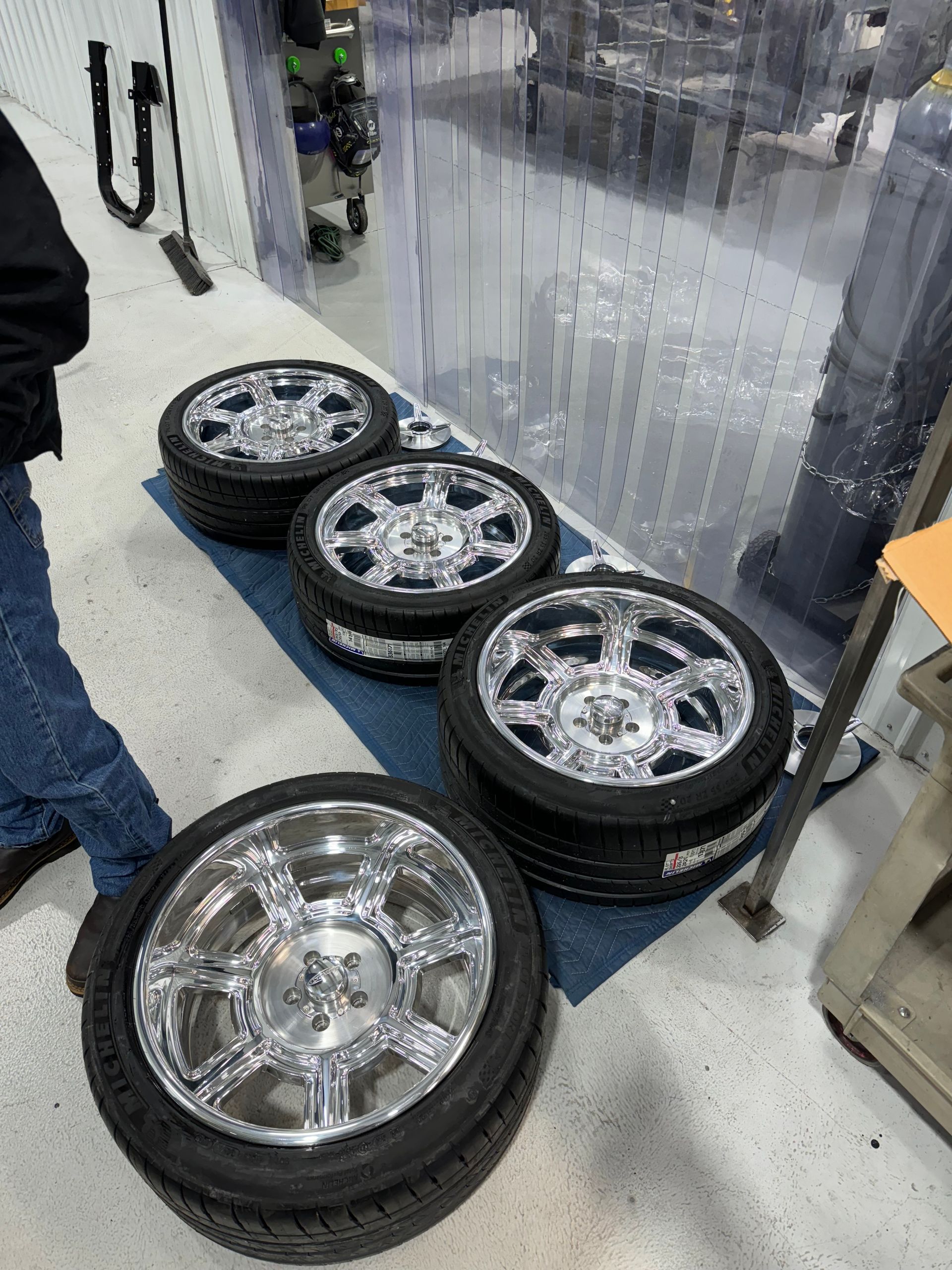 Five shiny chrome truck wheels with tires lined up on a shop floor