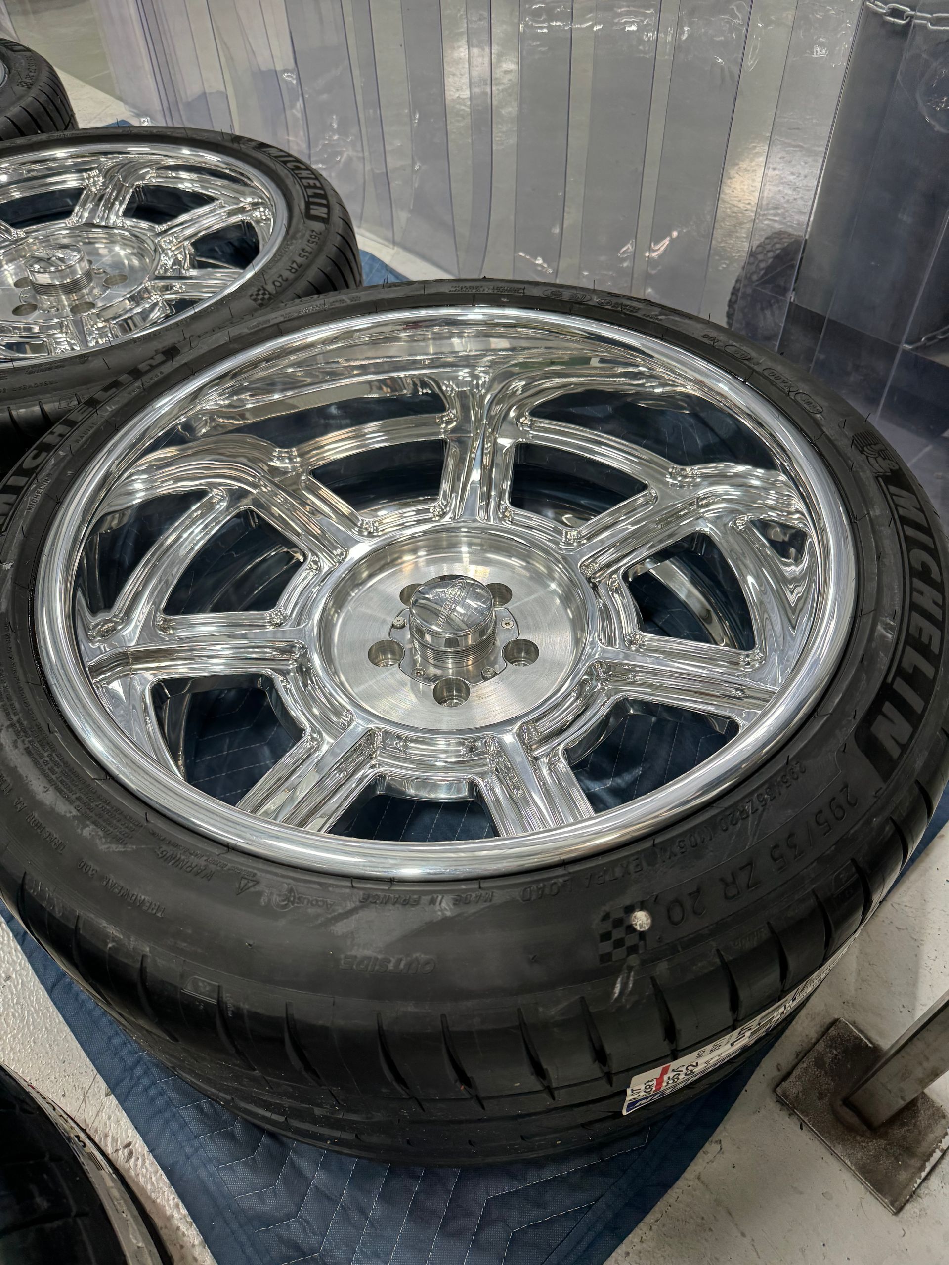Two shiny chrome rims with black tires leaning against a wall on a blue floor.