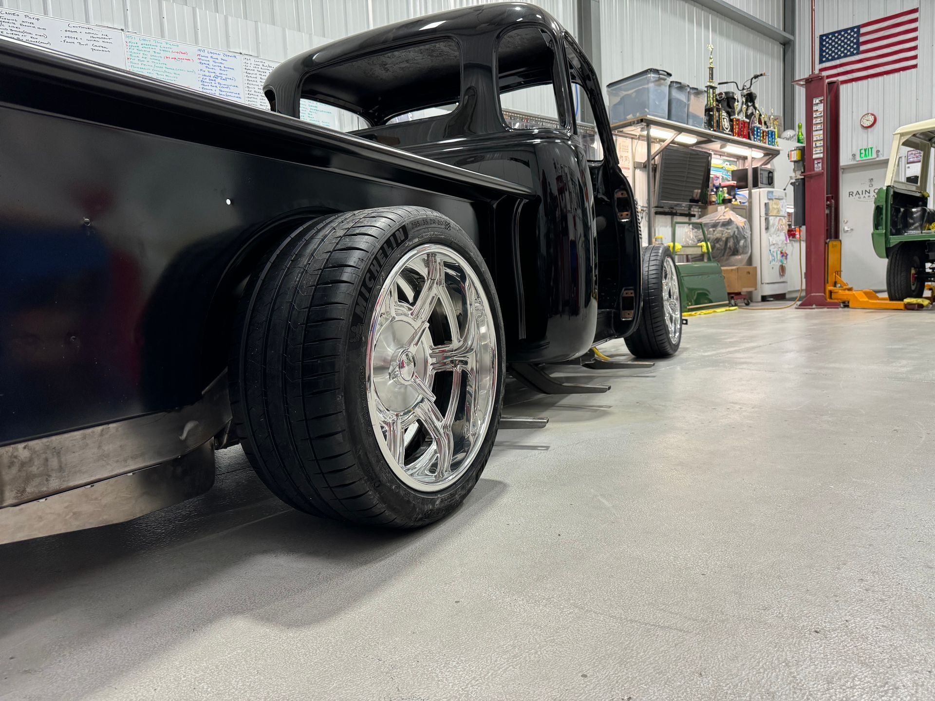 Custom black pickup truck in a garage, low-angle view of shiny chrome wheels and open shop interior