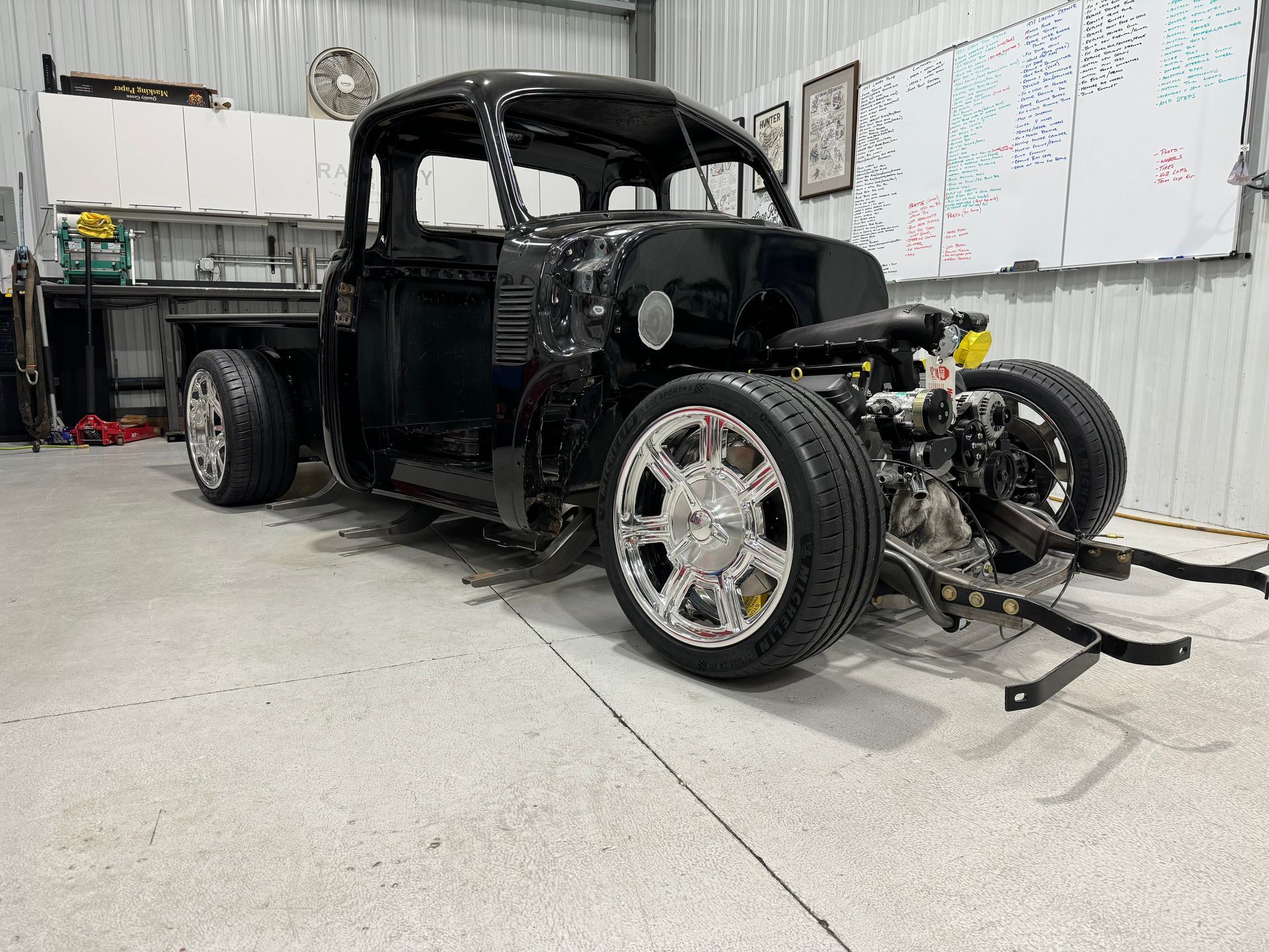 Black hot rod pickup in a garage, with exposed front wheels and chrome rims.