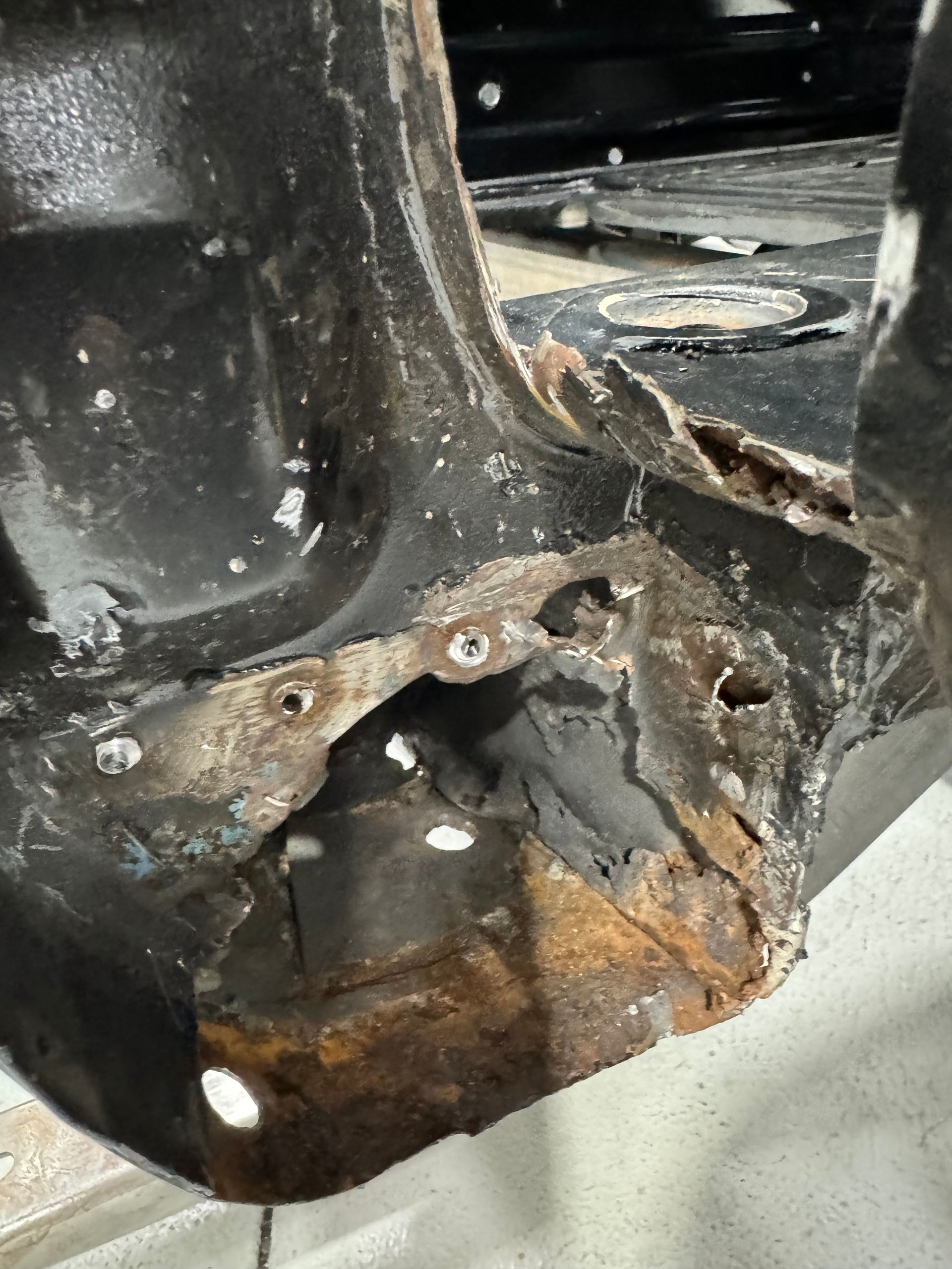 Close-up of a rusted, damaged metal bracket with holes and peeling black paint.
