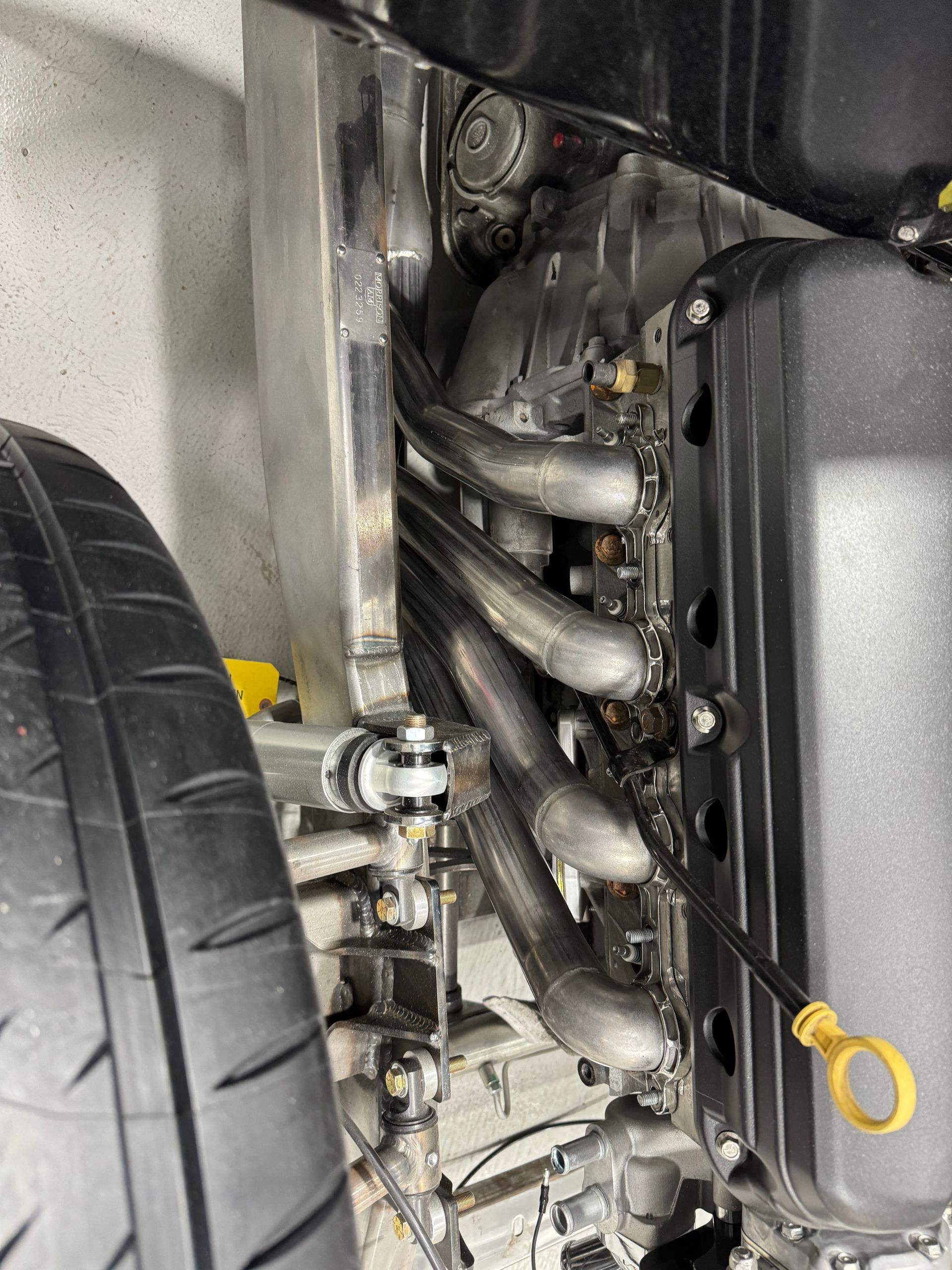 Close-up of a car engine bay with shiny exhaust pipes and the front tire visible.
