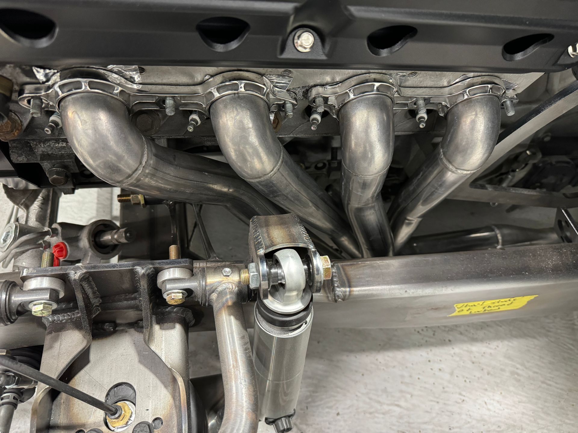 Car engine bay with polished metal exhaust headers and intake piping visible under the hood.
