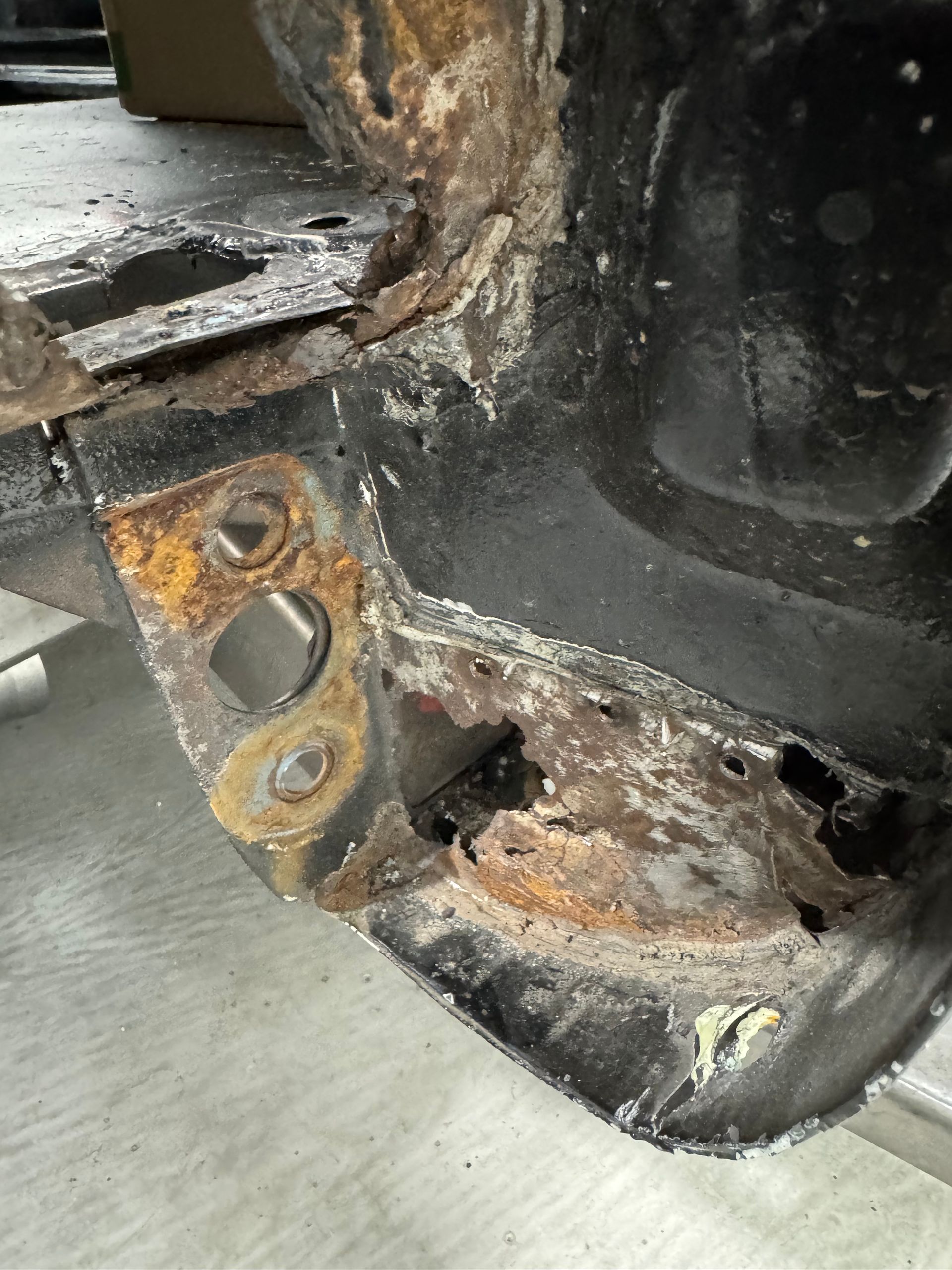 Rusty, corroded vehicle body panel with a damaged mounting bracket and holes near the wheel well.
