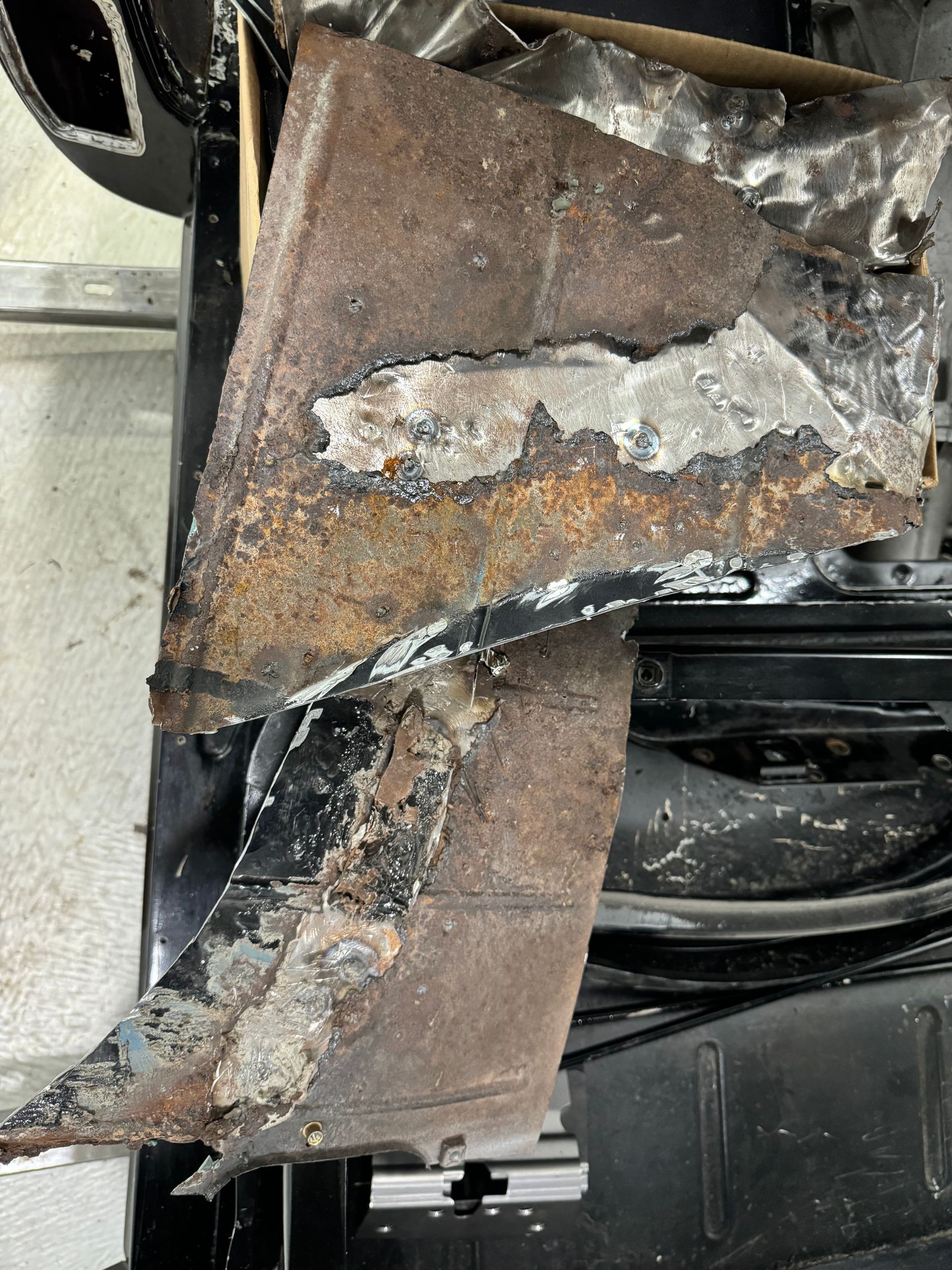 Severely rusted, corroded metal panel with peeling paint and bent edges on a vehicle underside