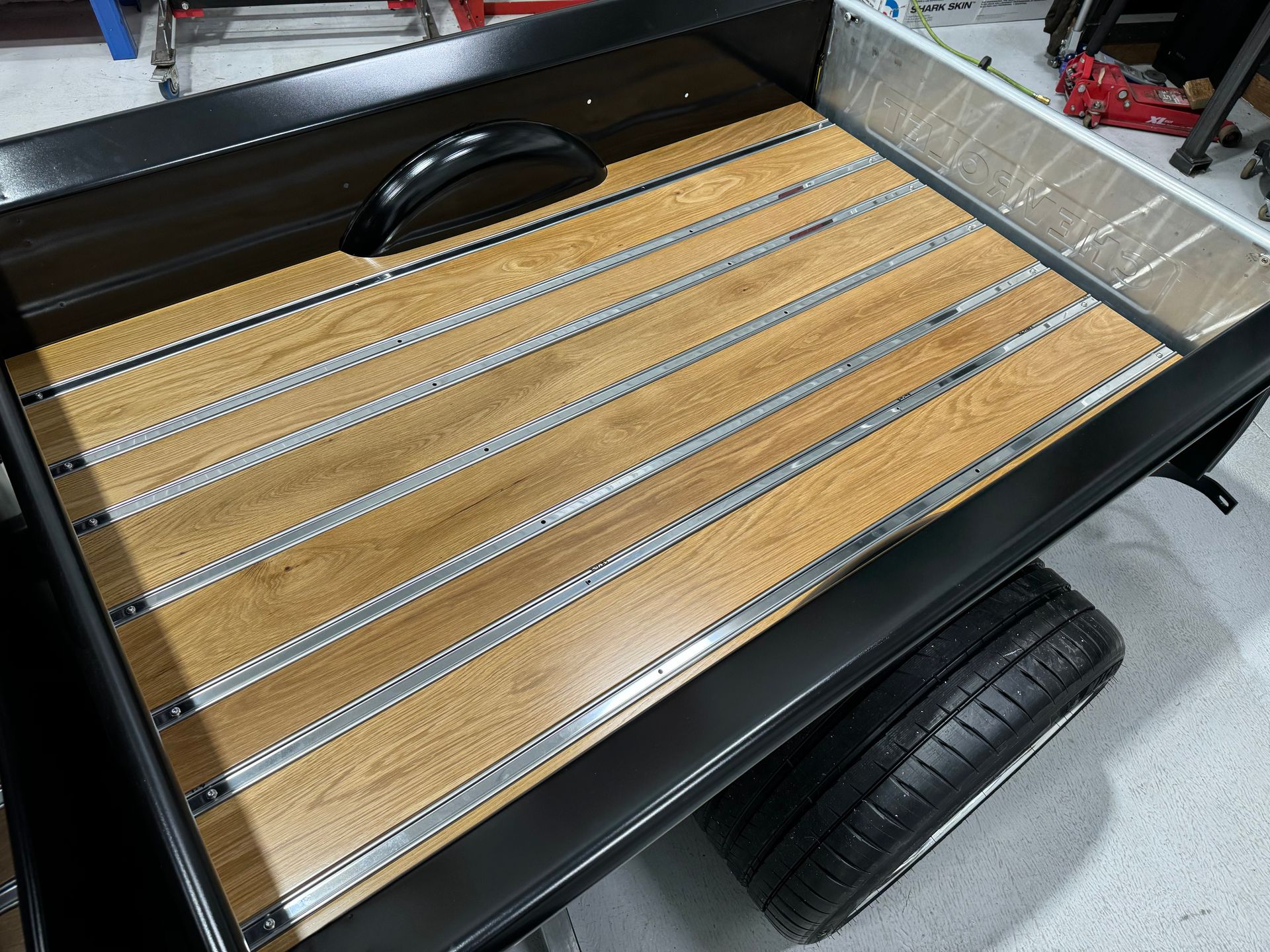 Black utility trailer bed with wooden slats and a visible wheel tire.