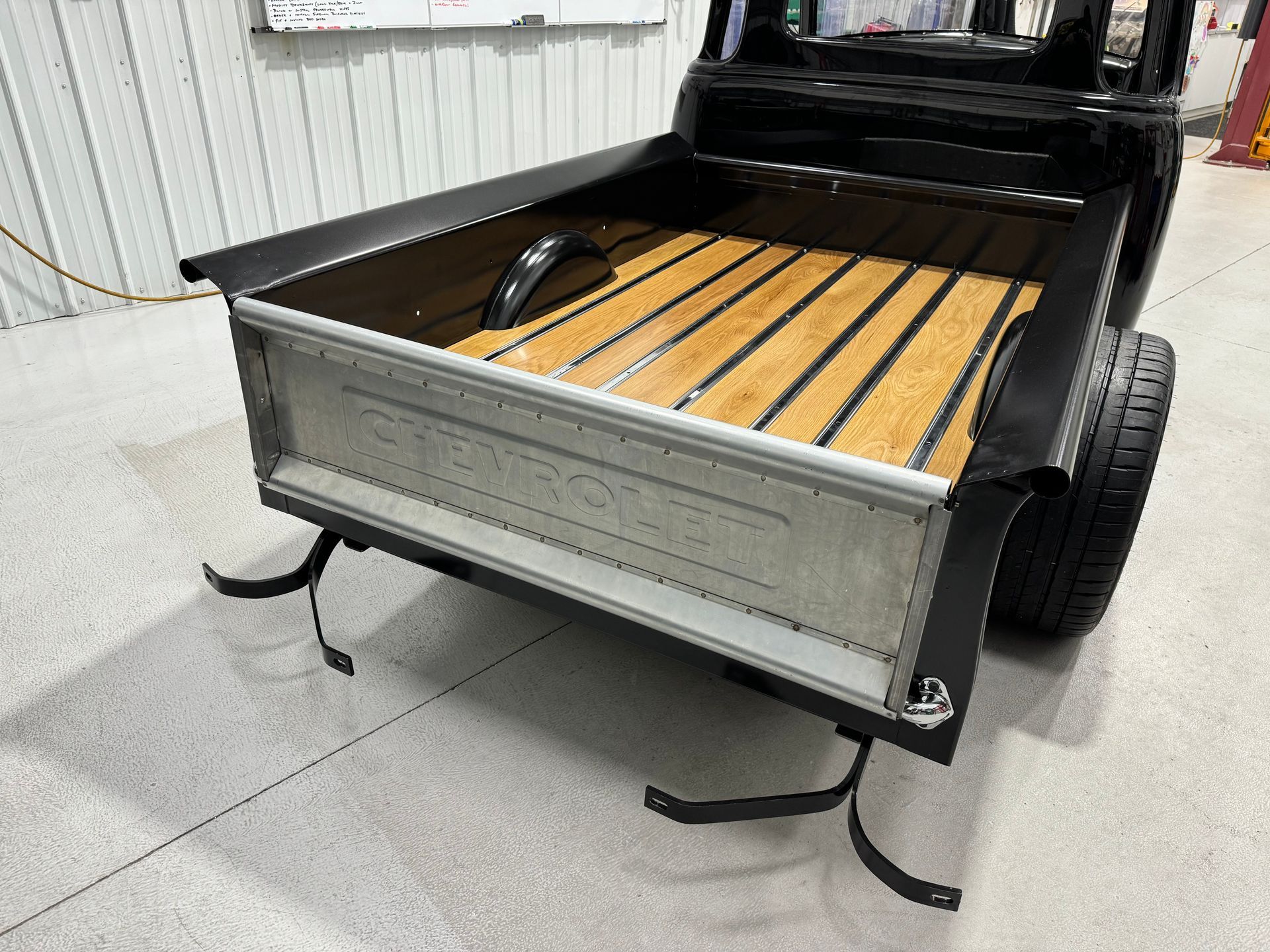 Vintage black pickup truck bed with wooden slats and shiny chrome tailgate in a garage.